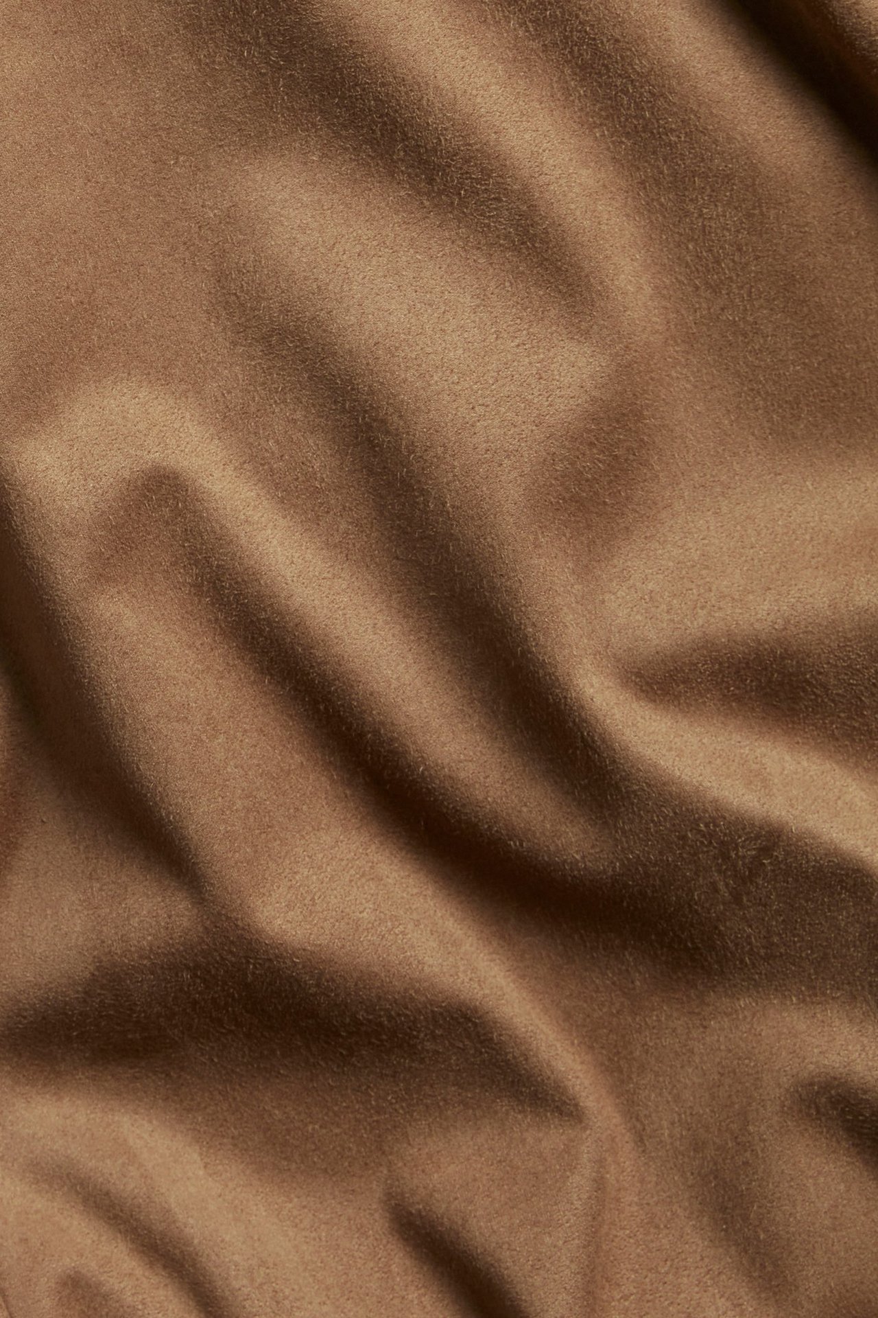 Zbliżenie na miękki brązowy zamszowy materiał na spódnicę z naturalnymi fałdami.