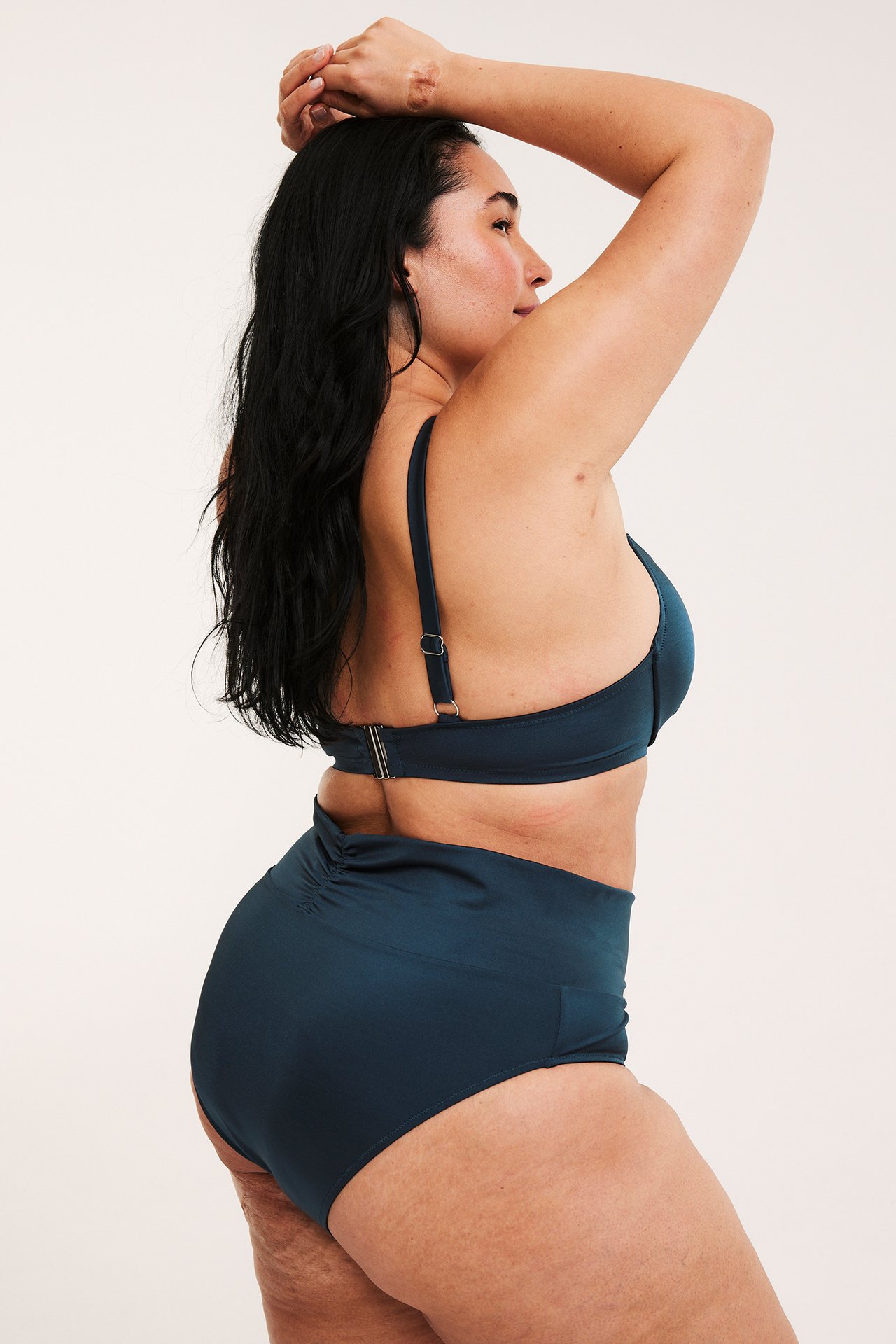 Widok z boku kobiety w granatowych figach kąpielowych z marszczeniem i pasującym topie bikini.