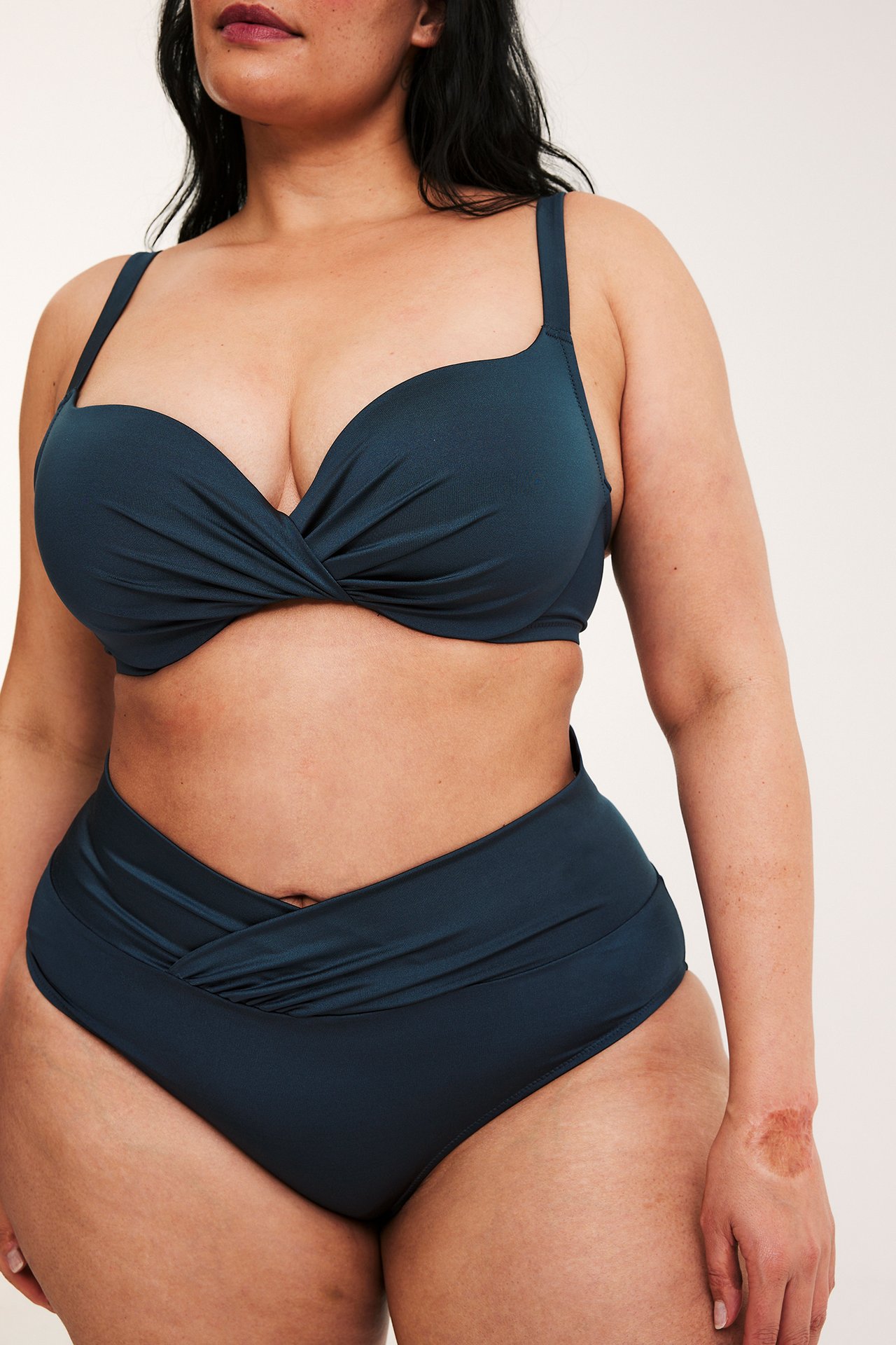 Widok z przodu: Kobieta w ciemnoniebieskich, drapowanych figach bikini i pasującej górze bikini.