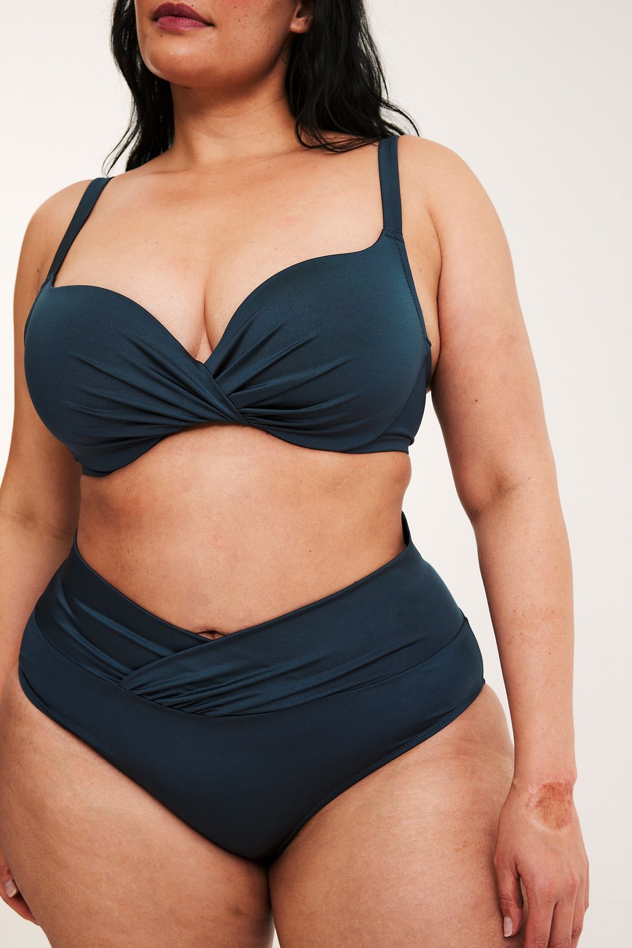 Frontvy: Kvinna i mörkblå draperad bikinitrosa och matchande vriden bikinitopp.