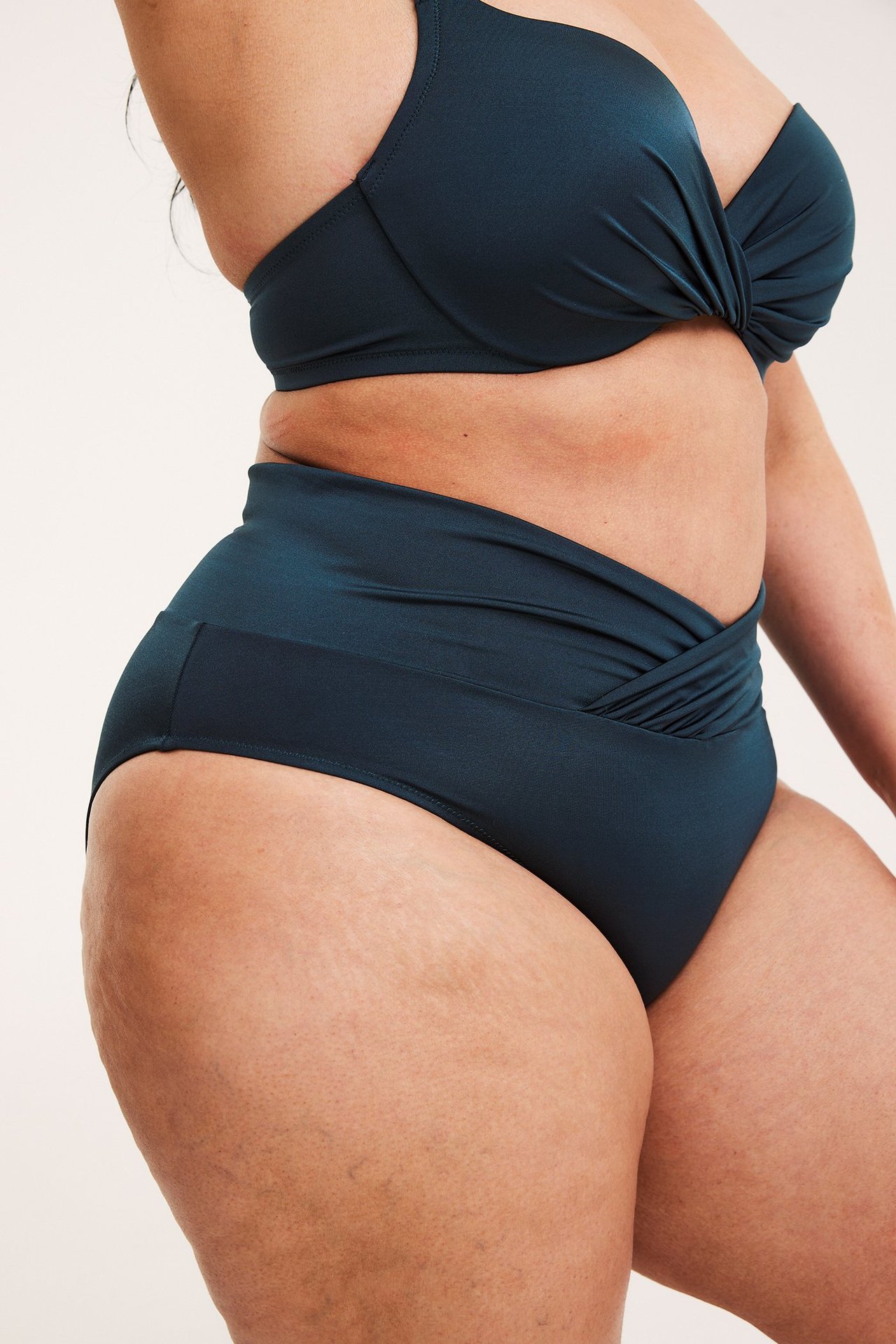 Widok z boku kobiety w ciemnoniebieskich majtkach bikini z wysokim stanem i drapowaniem oraz pasującym biustonoszu.
