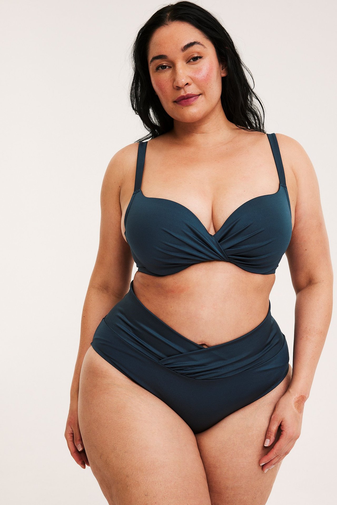 Framifrån, kvinna i mörkblå draperad bikinitrosa och matchande mörkblå bikinitopp.