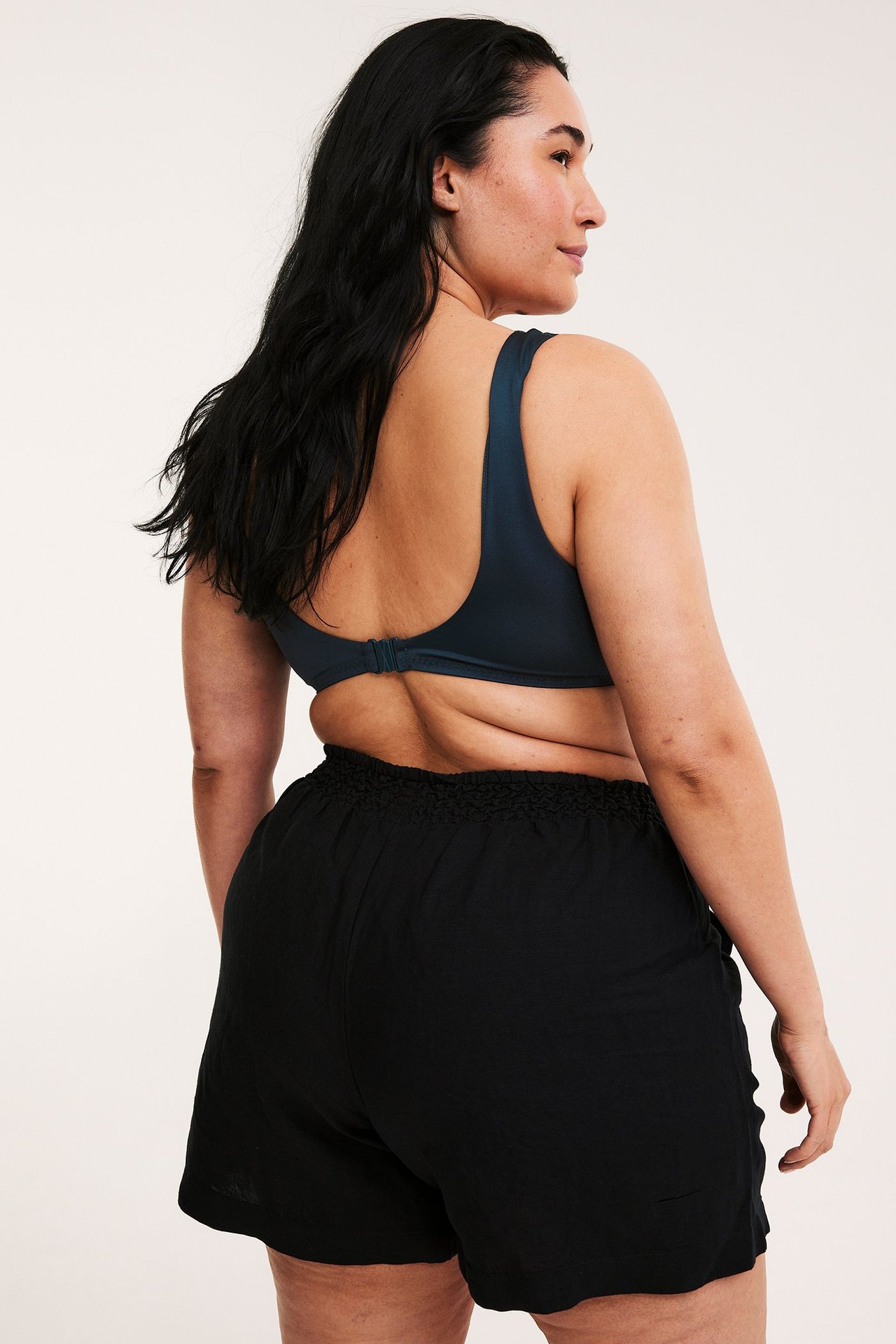 Bakifrån på kvinna i mörkblå vadderad bikini-bh med knäppe bak och svarta shorts.