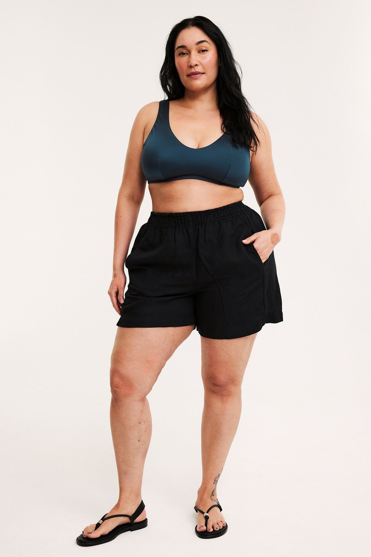 Framifrån: kvinna i mörkblå vadderad bikini-bh, svarta shorts och svarta sandaler.