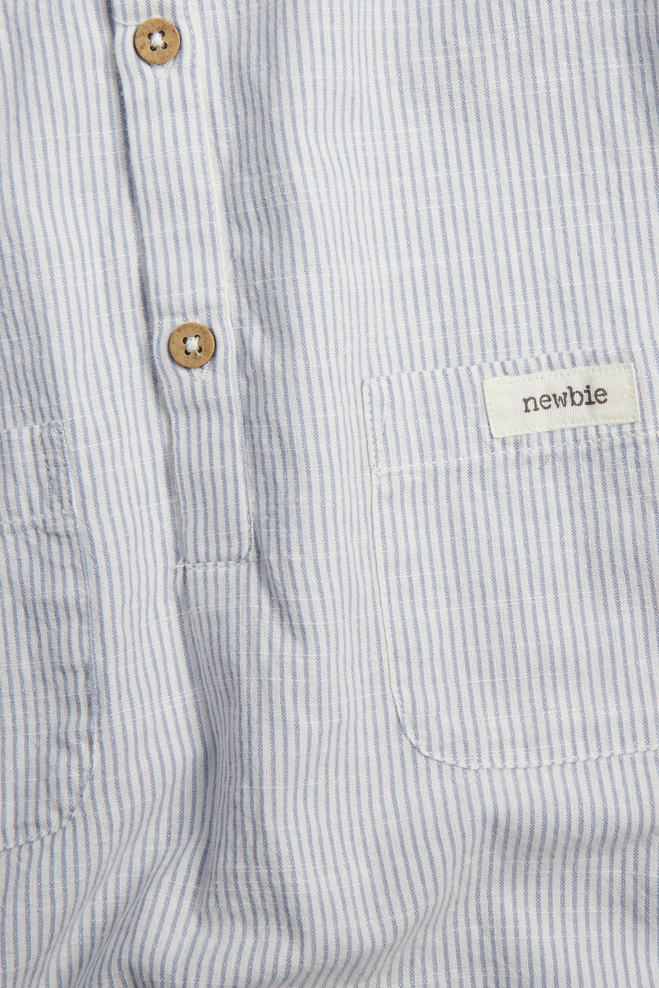 Zbliżenie na niebiesko-biały, pasiasty bawełniany rampers z drewnianymi guzikami i naszytą kieszenią.