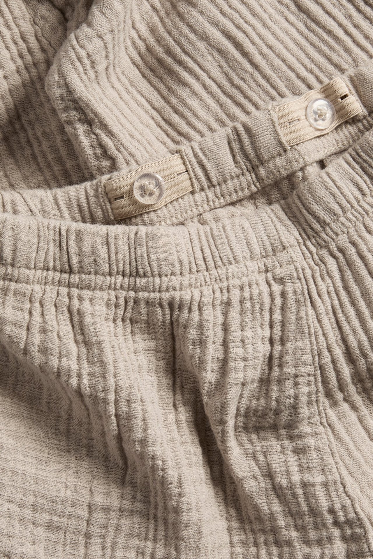 Zbliżenie na beżowe spodnie z muślinu z elastyczną talią i wewnętrzną regulowaną gumką z guzikami.