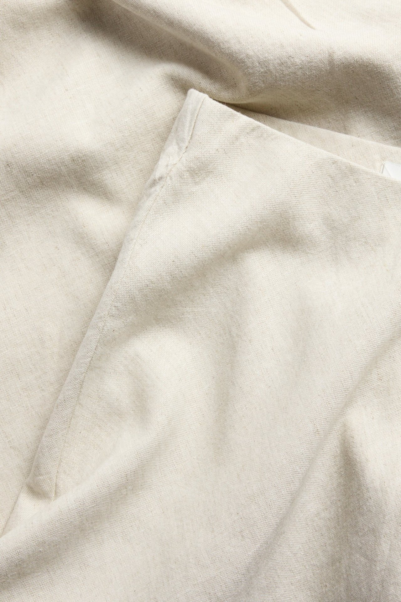 Zbliżenie beżowej tkaniny spódnicy midi z mieszanki lnu, ukazujące teksturę i fałdy.