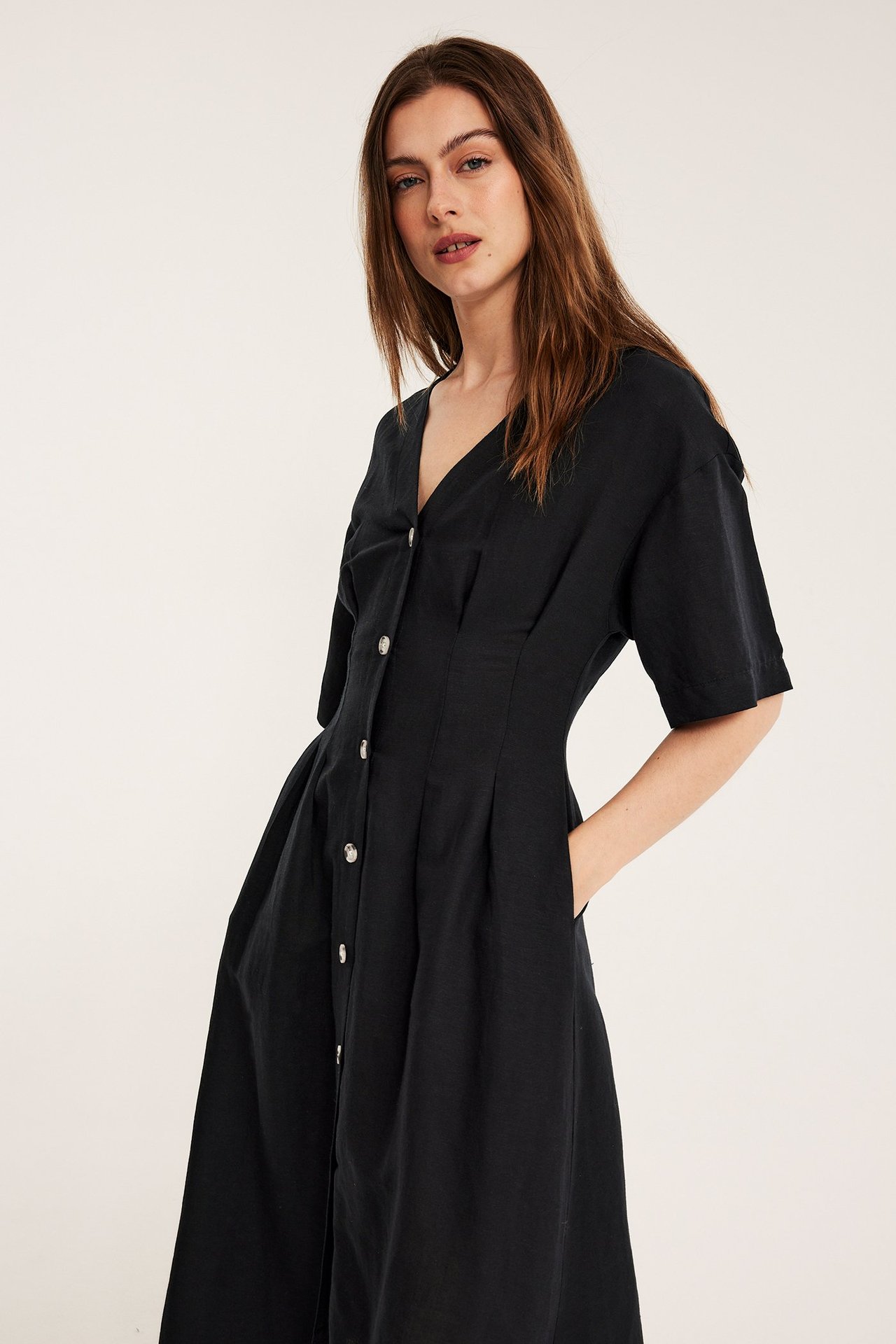 Edestäpäin, nainen mustassa pellavasekoitemekossa V-kauluksella, etunapeilla ja taskuilla.