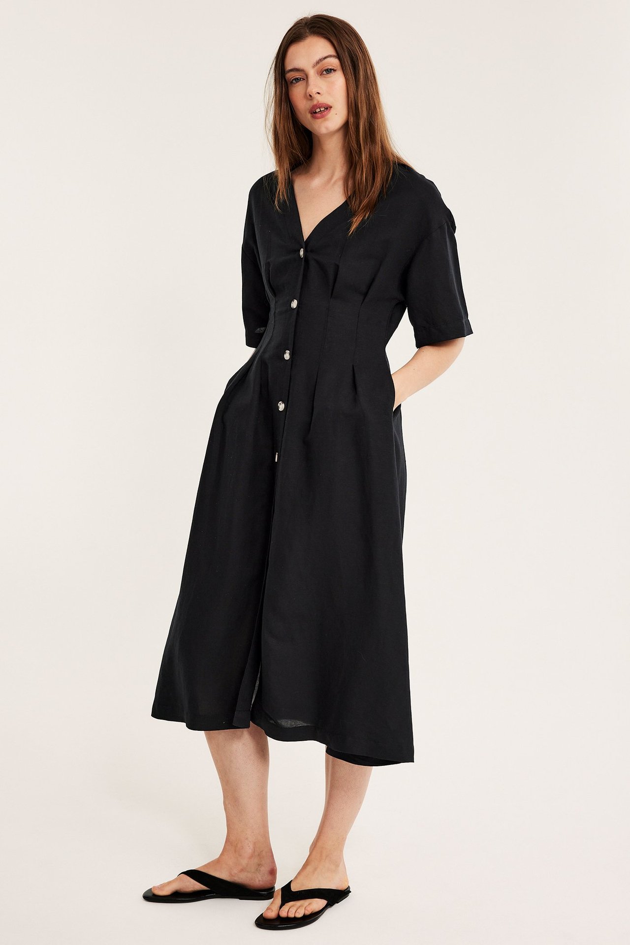 Edestä: nainen mustassa pellavasekoitemekossa napeilla ja mustissa varvassandaaleissa.