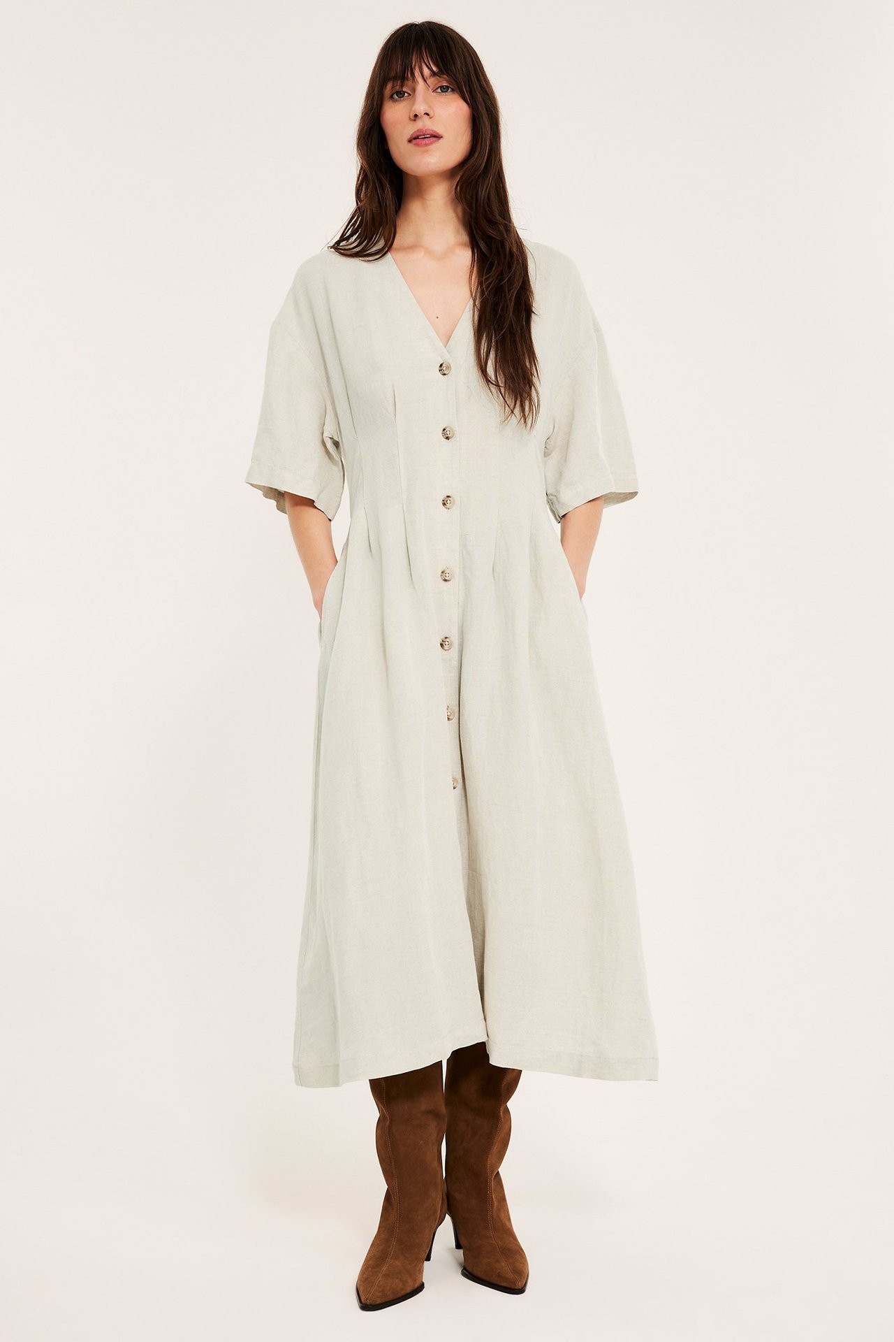 Etunäkymä: Nainen yllään vaaleanbeige pellavasekoitemekko etunapeilla ja ruskeilla mokkanahkasaappailla.