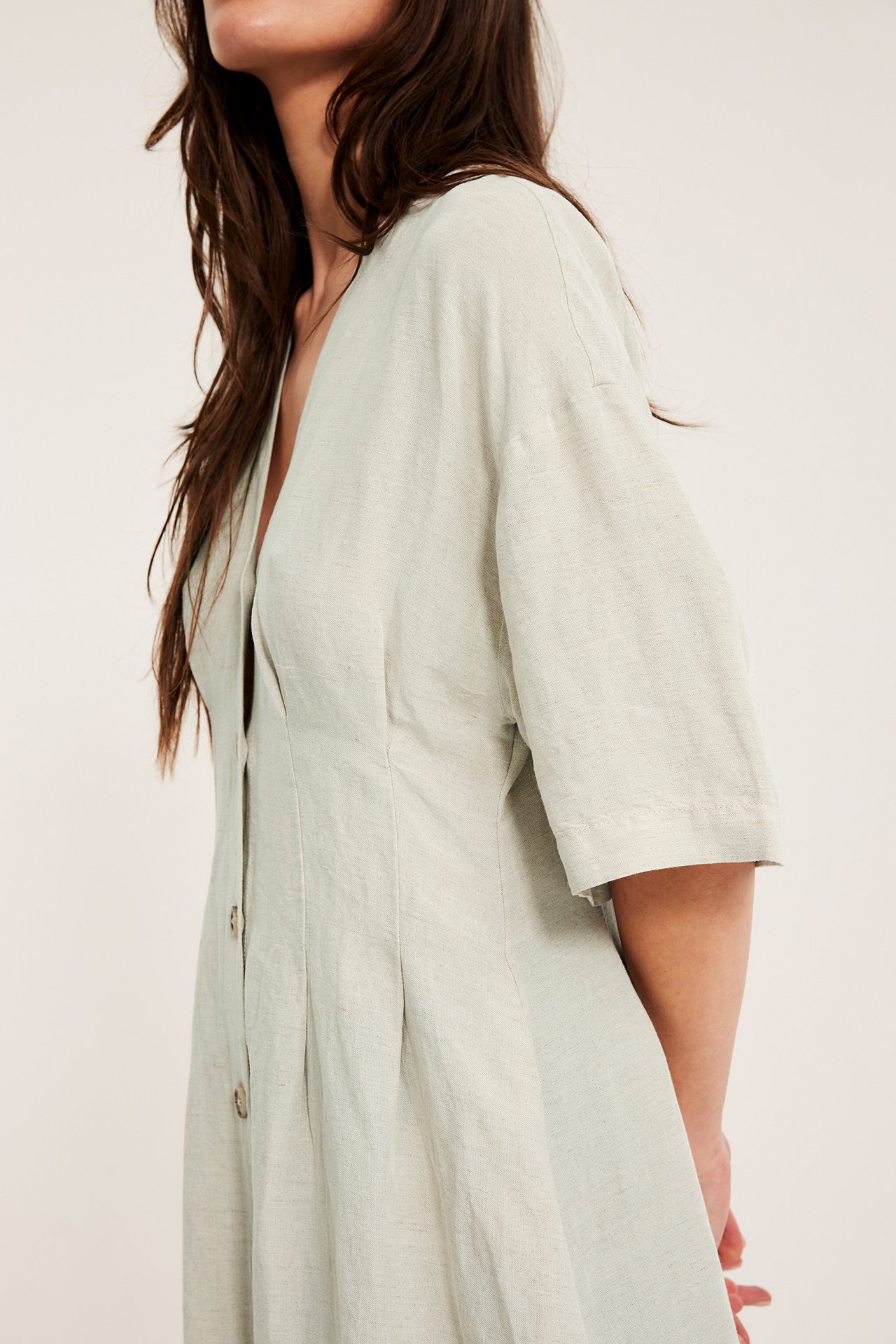 Lähikuva naisesta beige pellavasekoitemekko V-pääntiellä ja nappikiinnityksellä edessä.