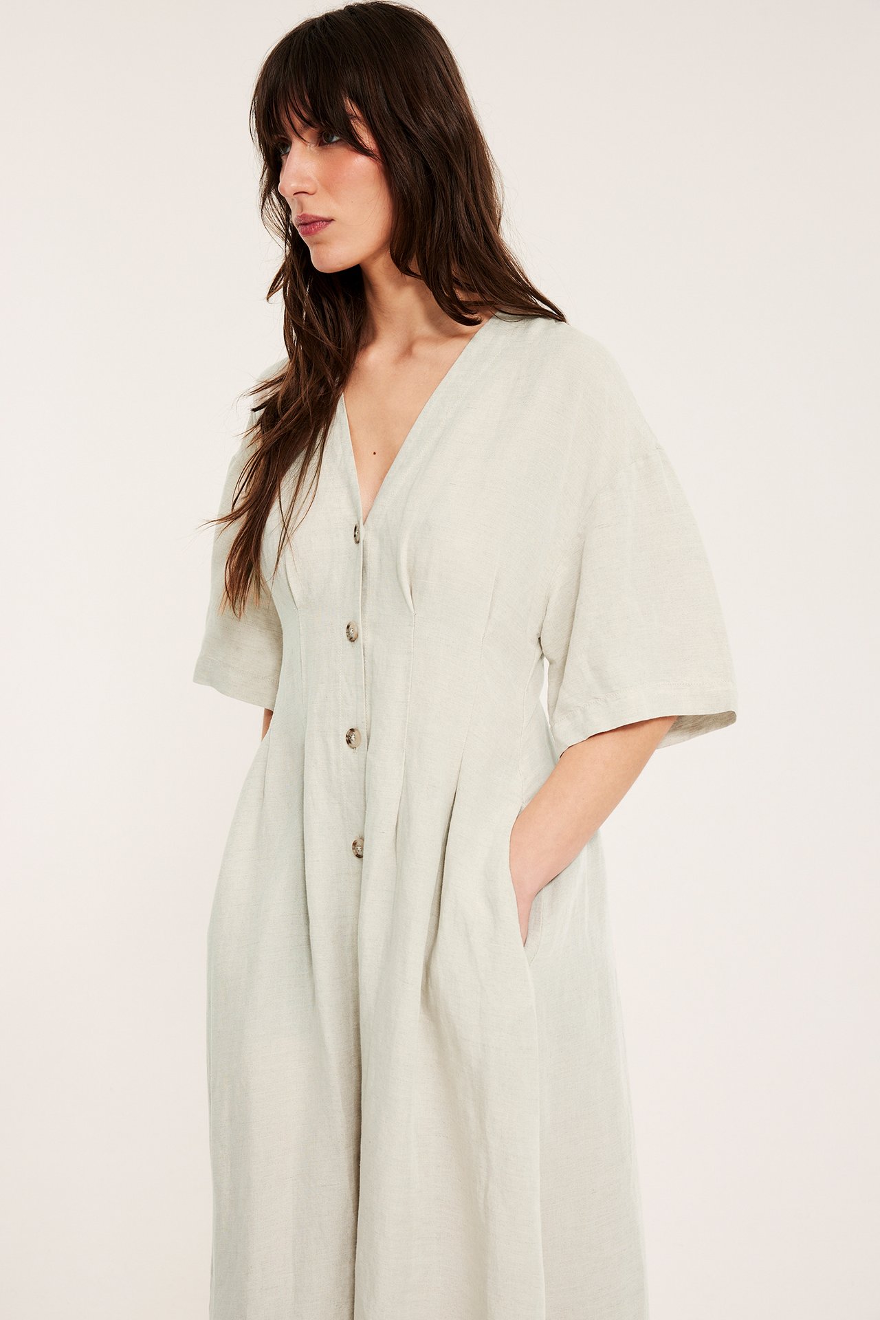 Edestä: Nainen beigen pellavasekoitemekossa, jossa V-pääntie, napit edessä, kiristetty vyötärö, lyhyet leveät hihat.