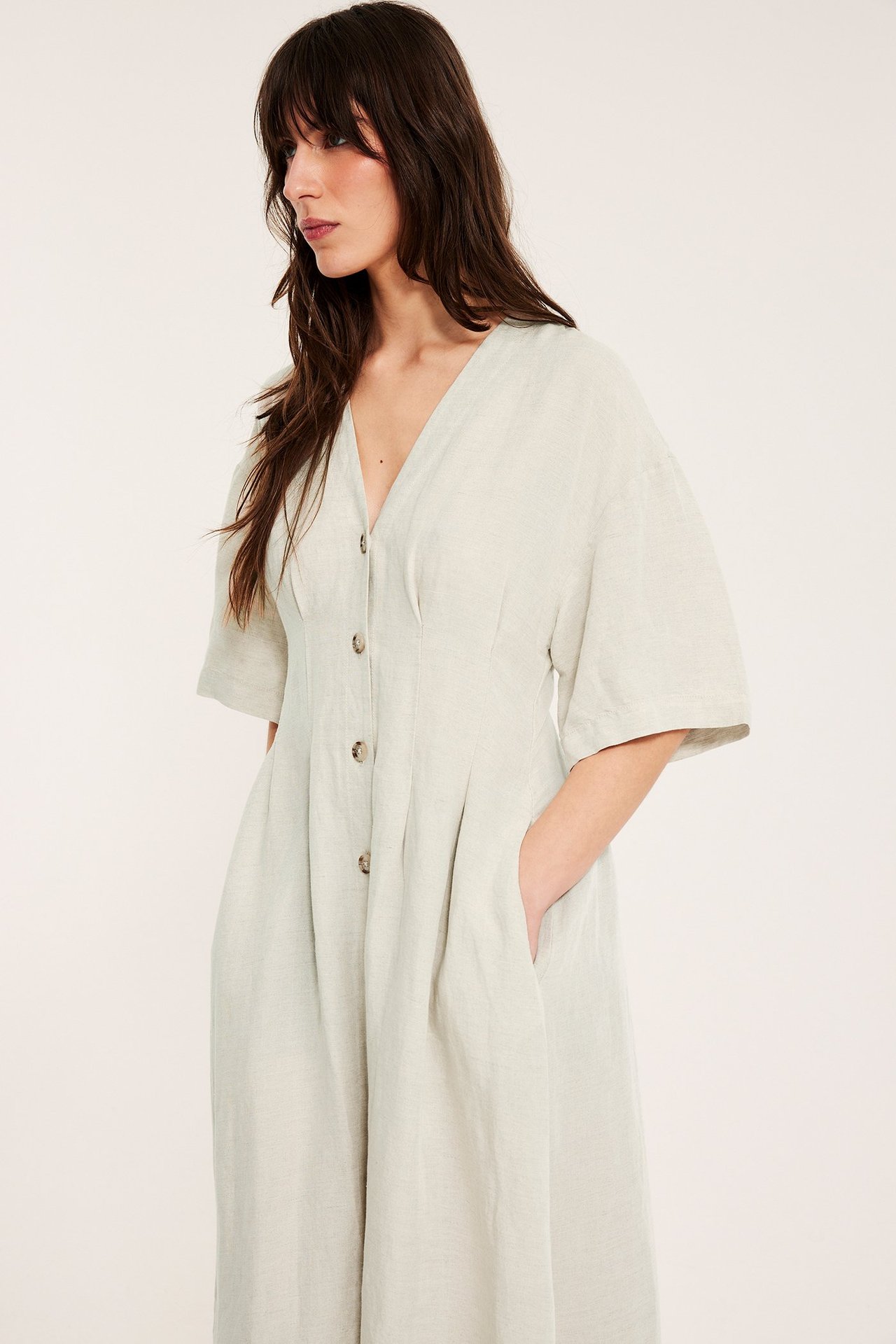 Edestä: Nainen beigen pellavasekoitemekossa, jossa V-pääntie, napit edessä, kiristetty vyötärö, lyhyet leveät hihat.