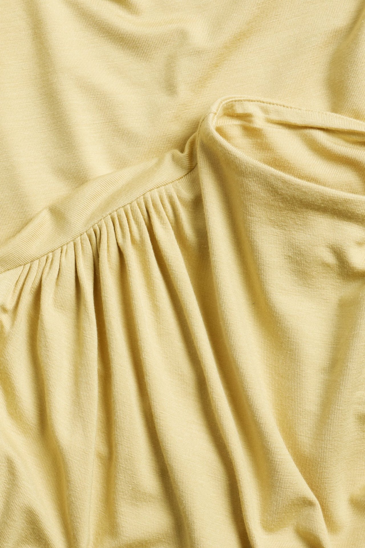 Zbliżenie na jasny żółty, długi rękaw, wiskozowy top z drapowaniem i marszczeniami.