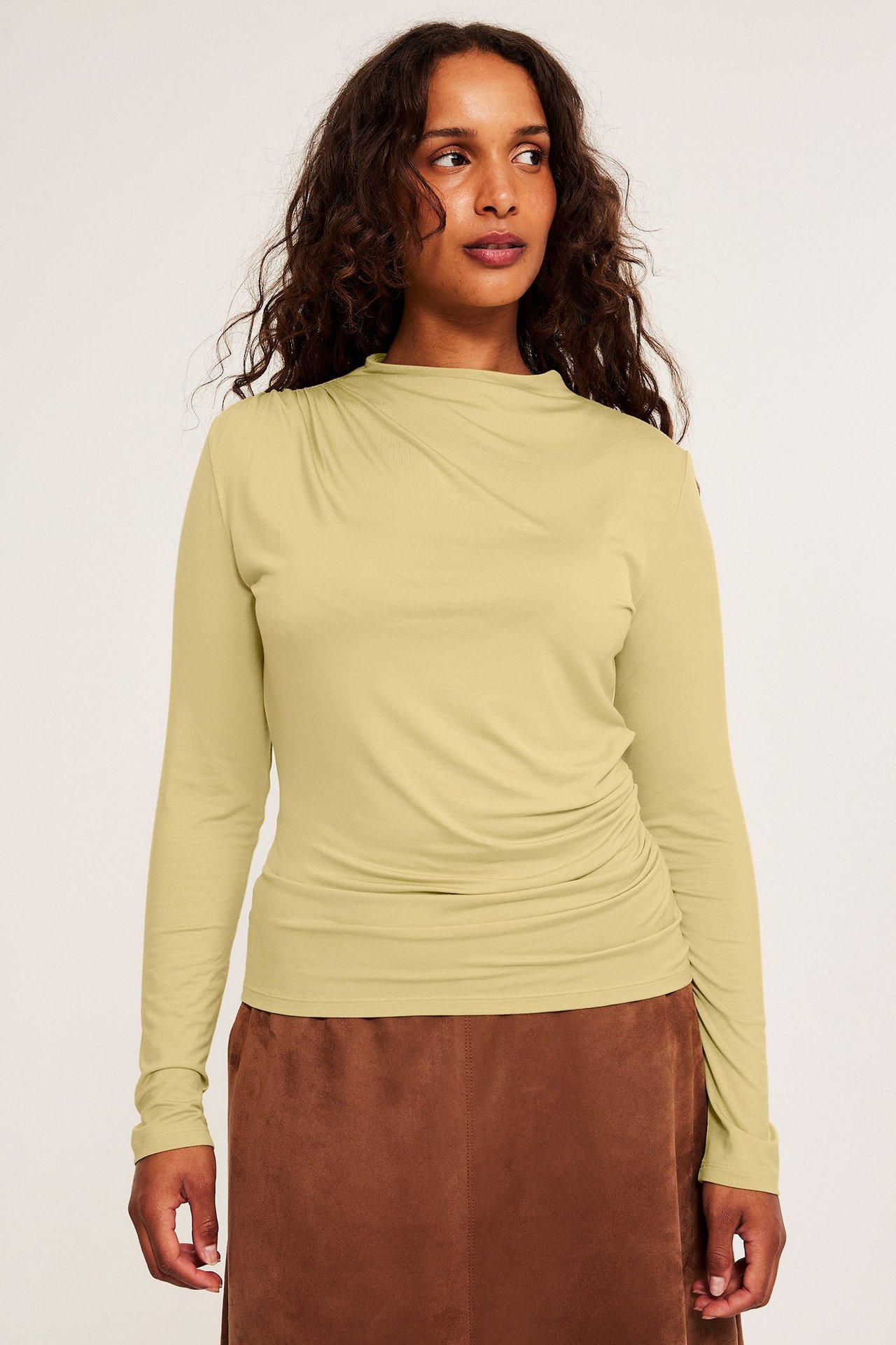 Frontbilde av en kvinne i en lys gul langermet viskosetopp med elegant drapering og et brunt skjørt.