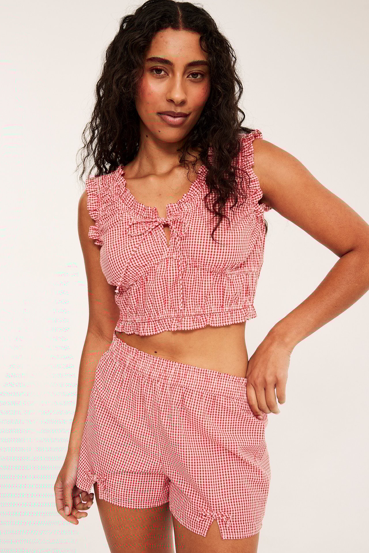Nainen punaisessa ruudullisessa puuvillapyjamassa: röyhelöinen crop-toppi ja shortsit, edestä.
