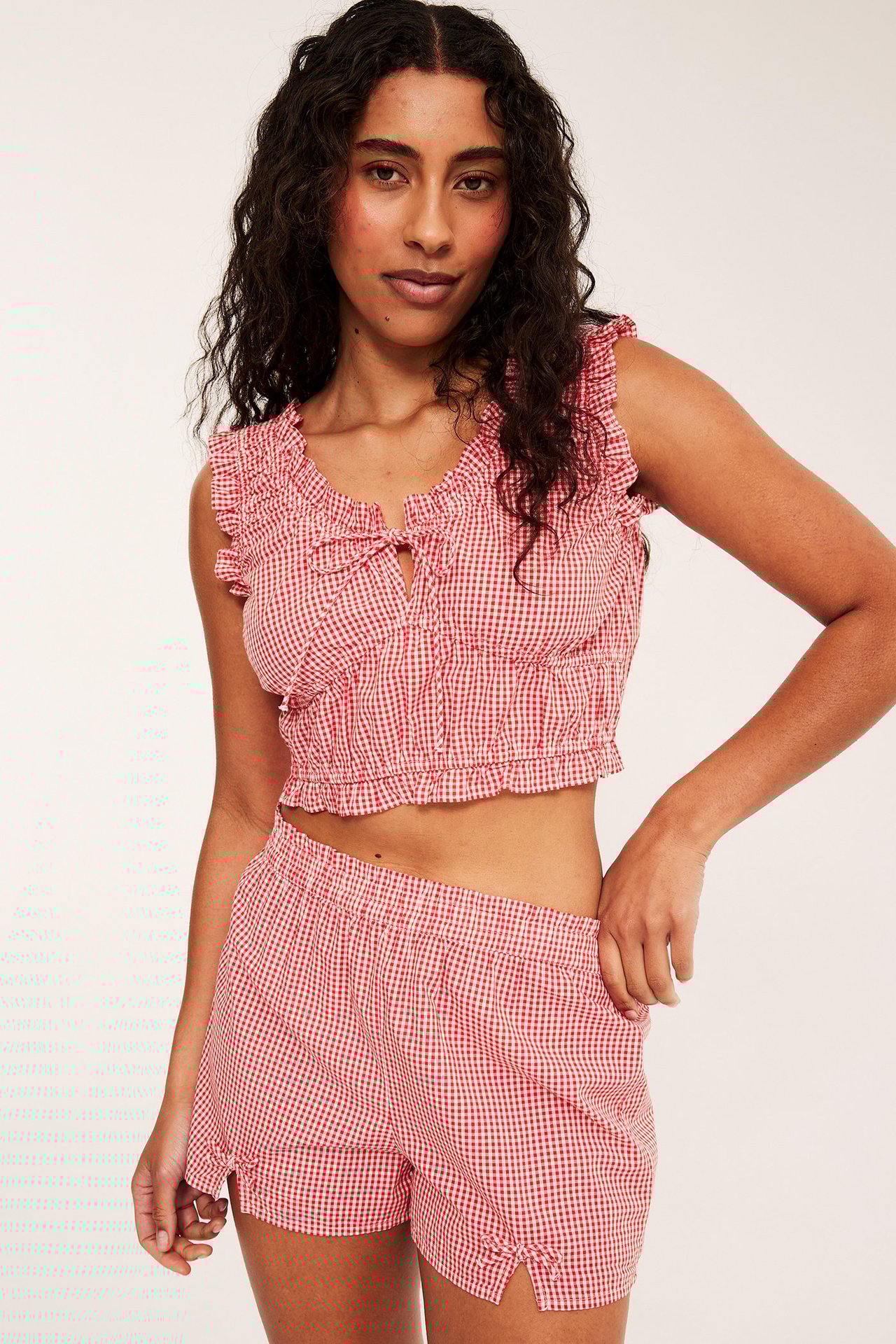 Frontvy av kvinna i rött rutigt pyjamasset i bomullspoplin med volangprydd croptop och shorts.