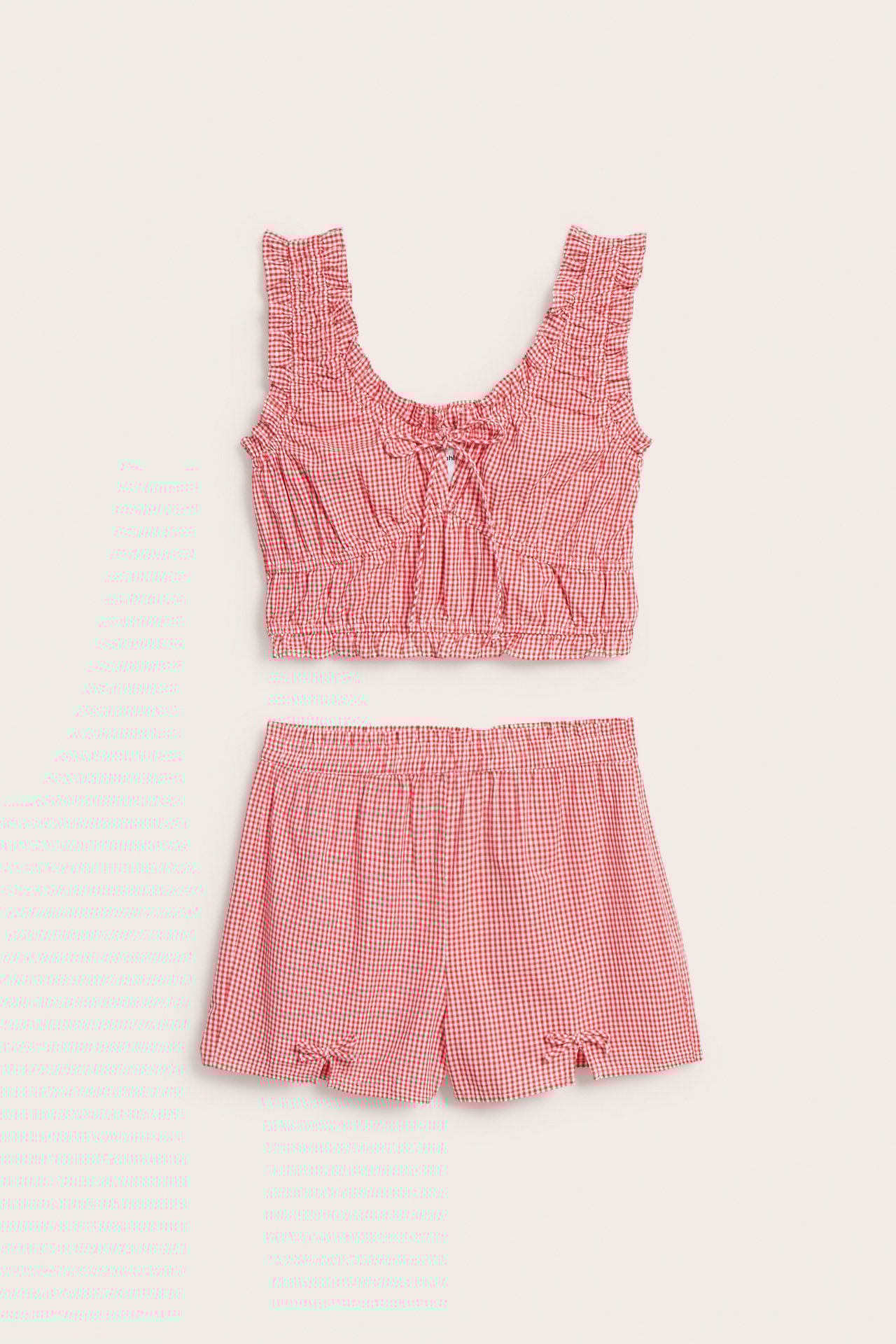 Forfra: Rødt og hvitt rutete pysjamassett i bomull. Volangkantet topp med knyting; shorts med strikk og sløyfer.