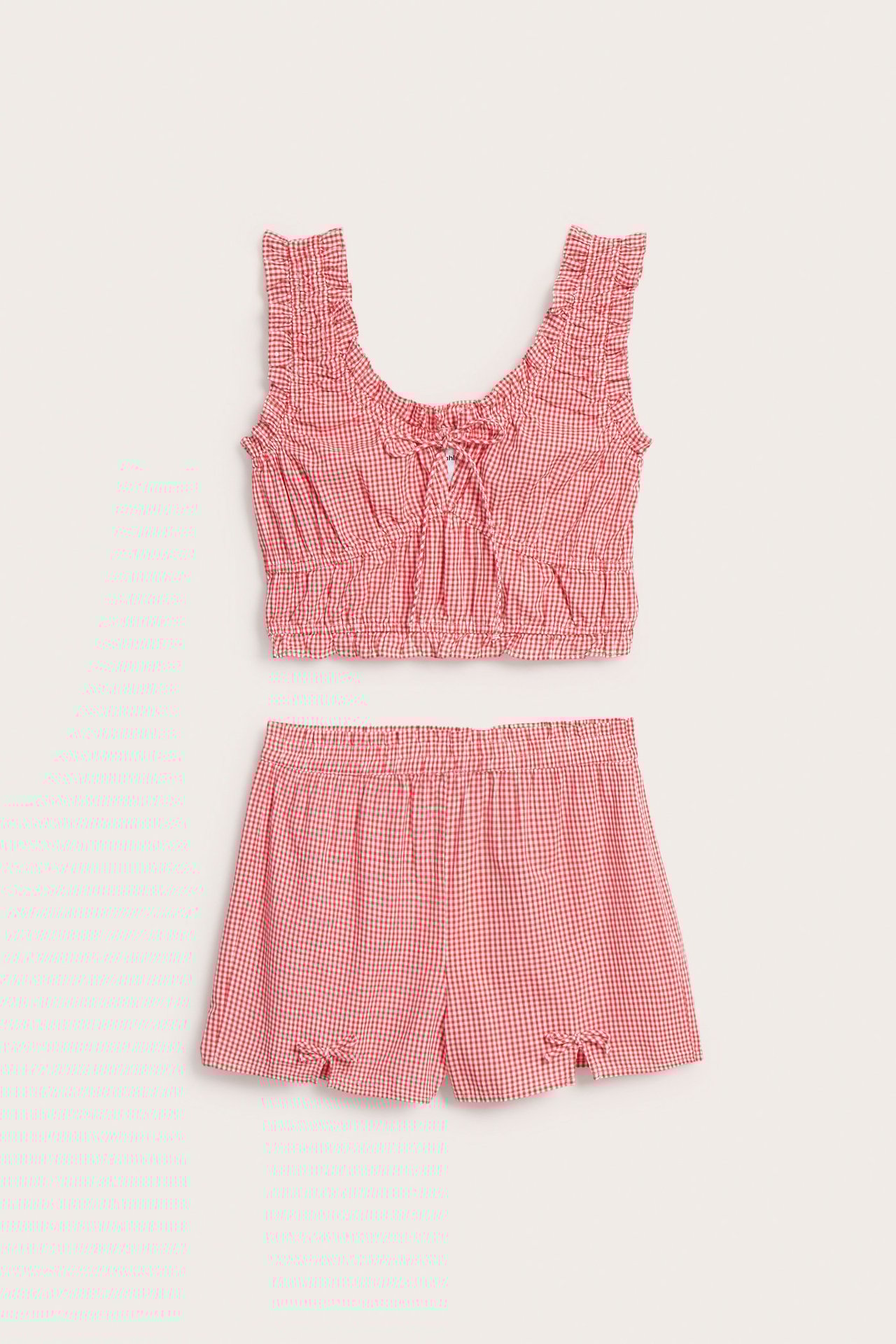 Framsida: Röd- och vitrutigt pyjamasset i bomull. Volangkantad topp med knytning; resårshorts med rosetter.