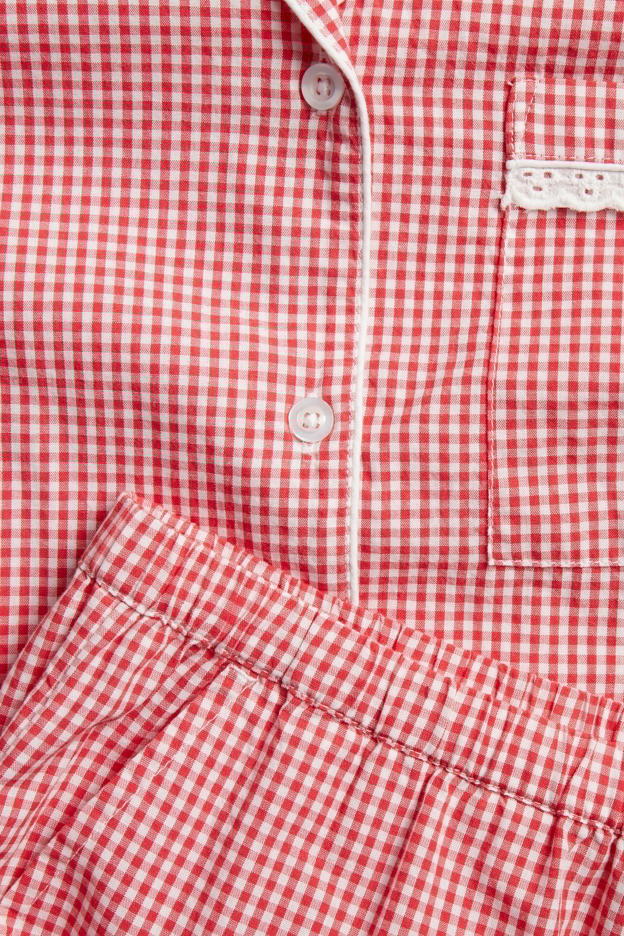 Nærbilde: rød og hvitrutet pyjamastopp i bomullspoplin med hvite kantdetaljer og brystlomme, samt matchende shorts.