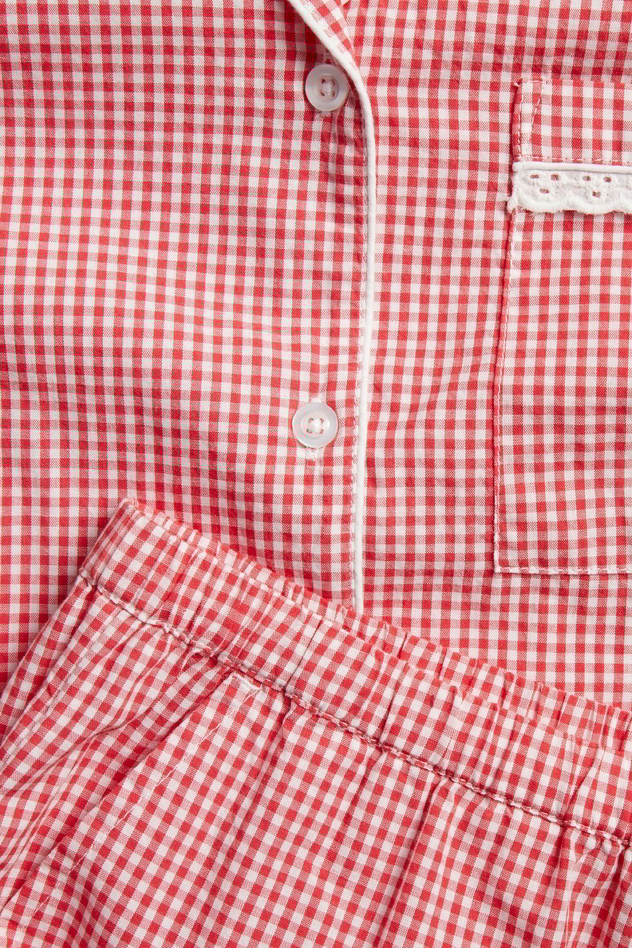 Zbliżenie: czerwona koszula piżamowa w kratę z białą lamówką i kieszenią, oraz pasujące szorty.