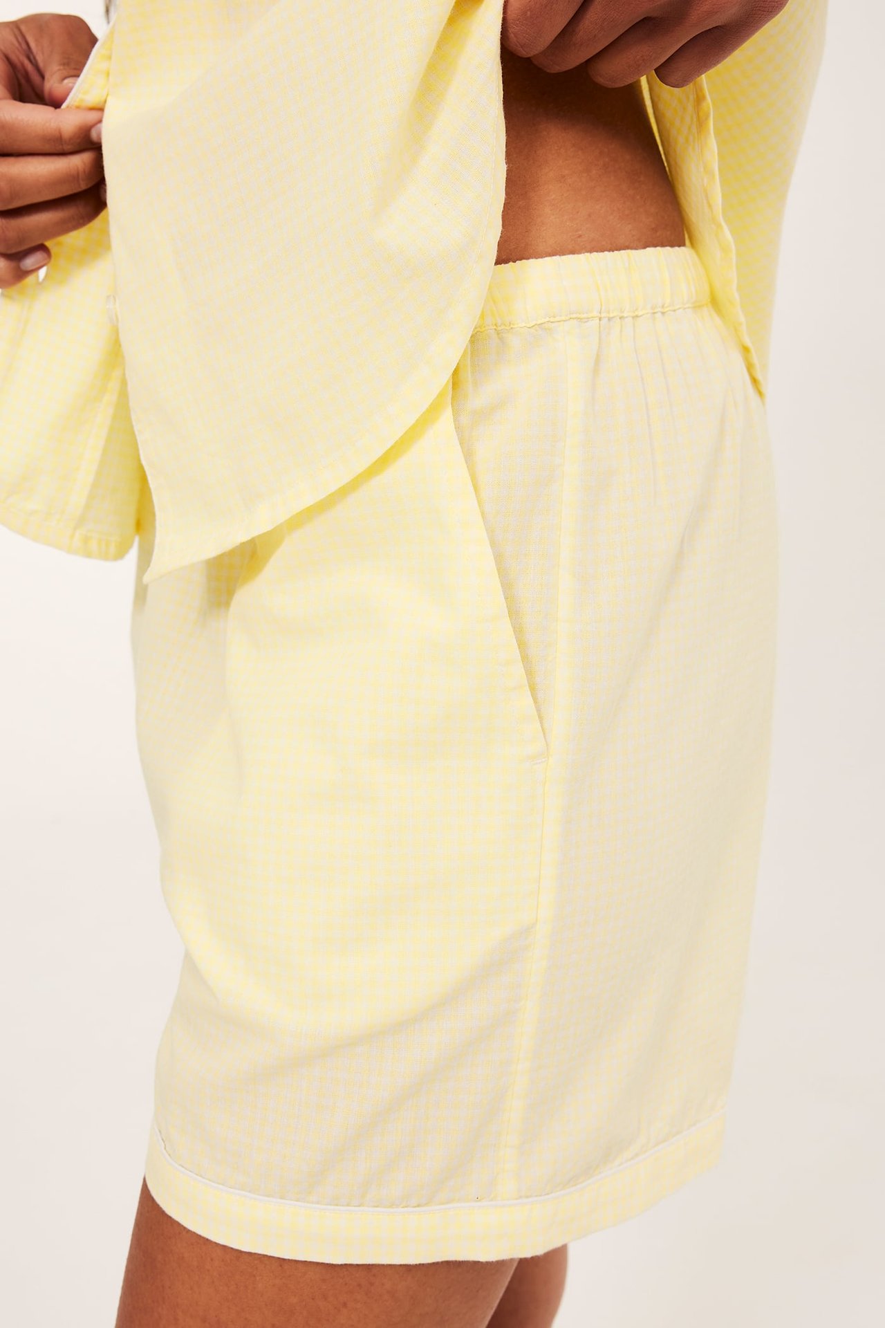 Sivukuva naisesta yllään vaaleanbeiget ruudulliset puuvillapyjamashortsit taskuilla ja yhteensopiva yläosa.