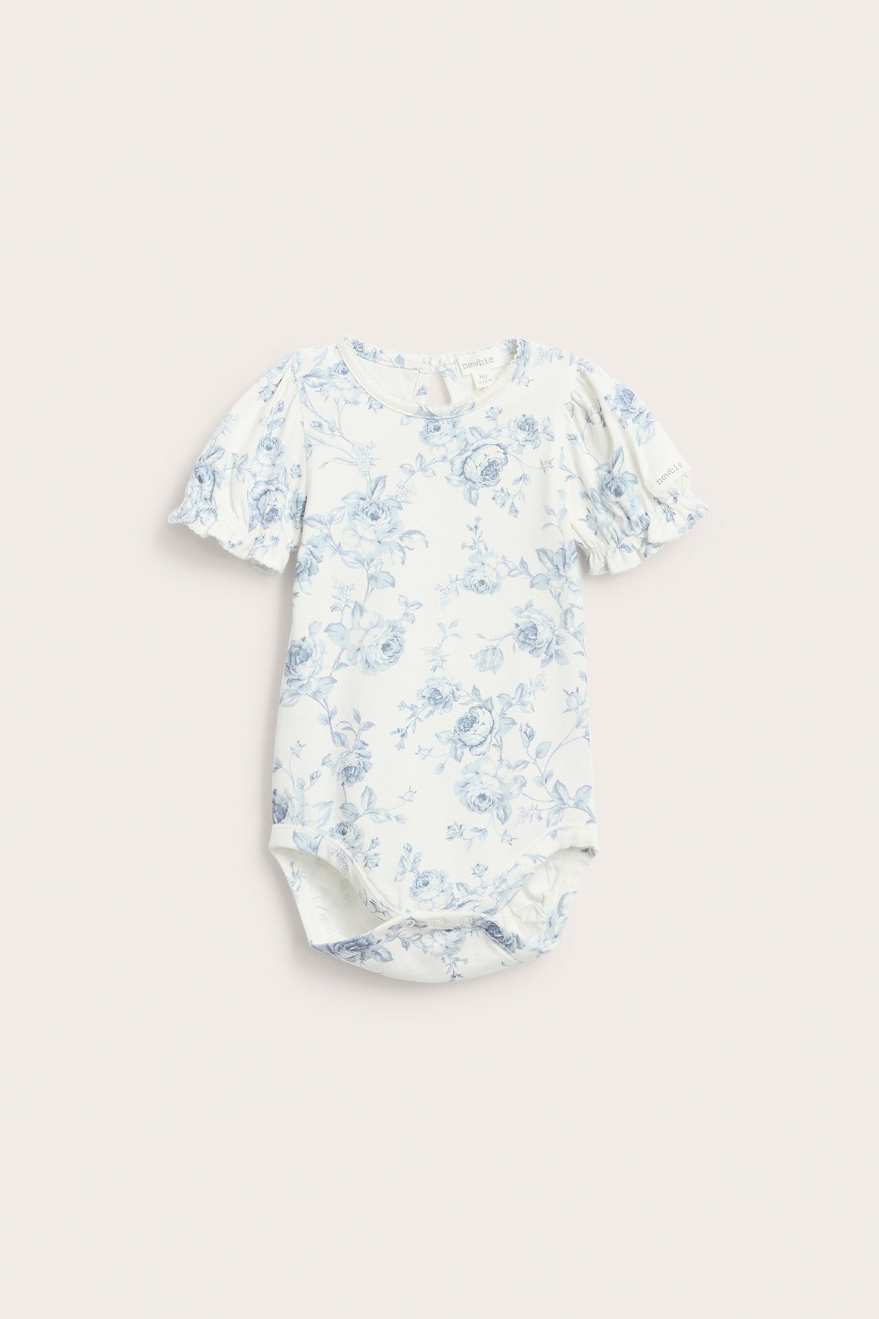 Frontvisning: Offwhite babybody med blått blomstermønster, korte puffermer, elastiske mansjetter og picotkant.