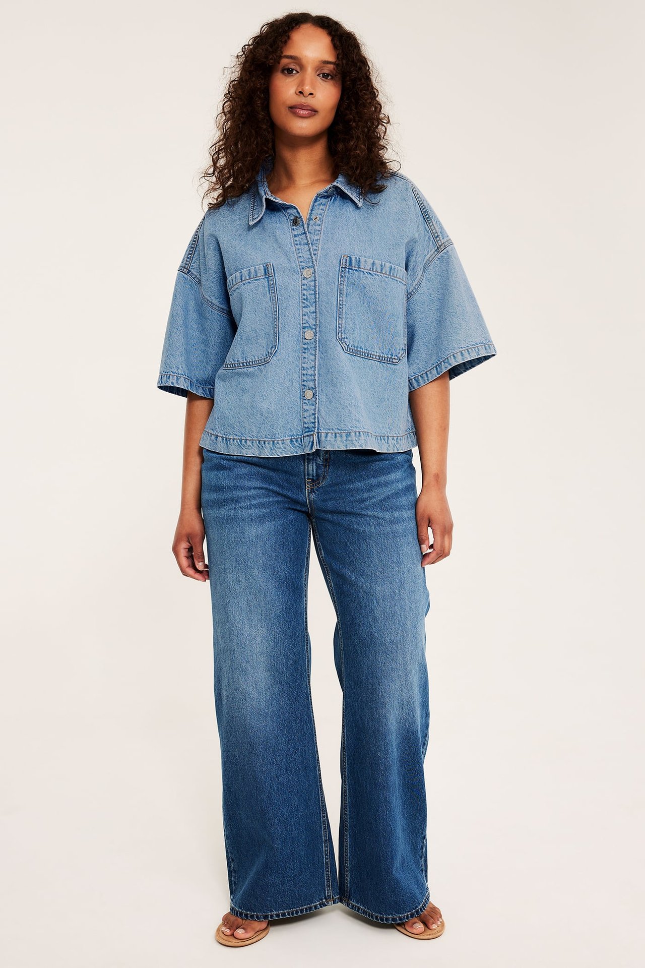 Framifrån: kvinna i ljusblå kort jeansskjorta, mörkblå vida jeans och ljusbruna sandaler.