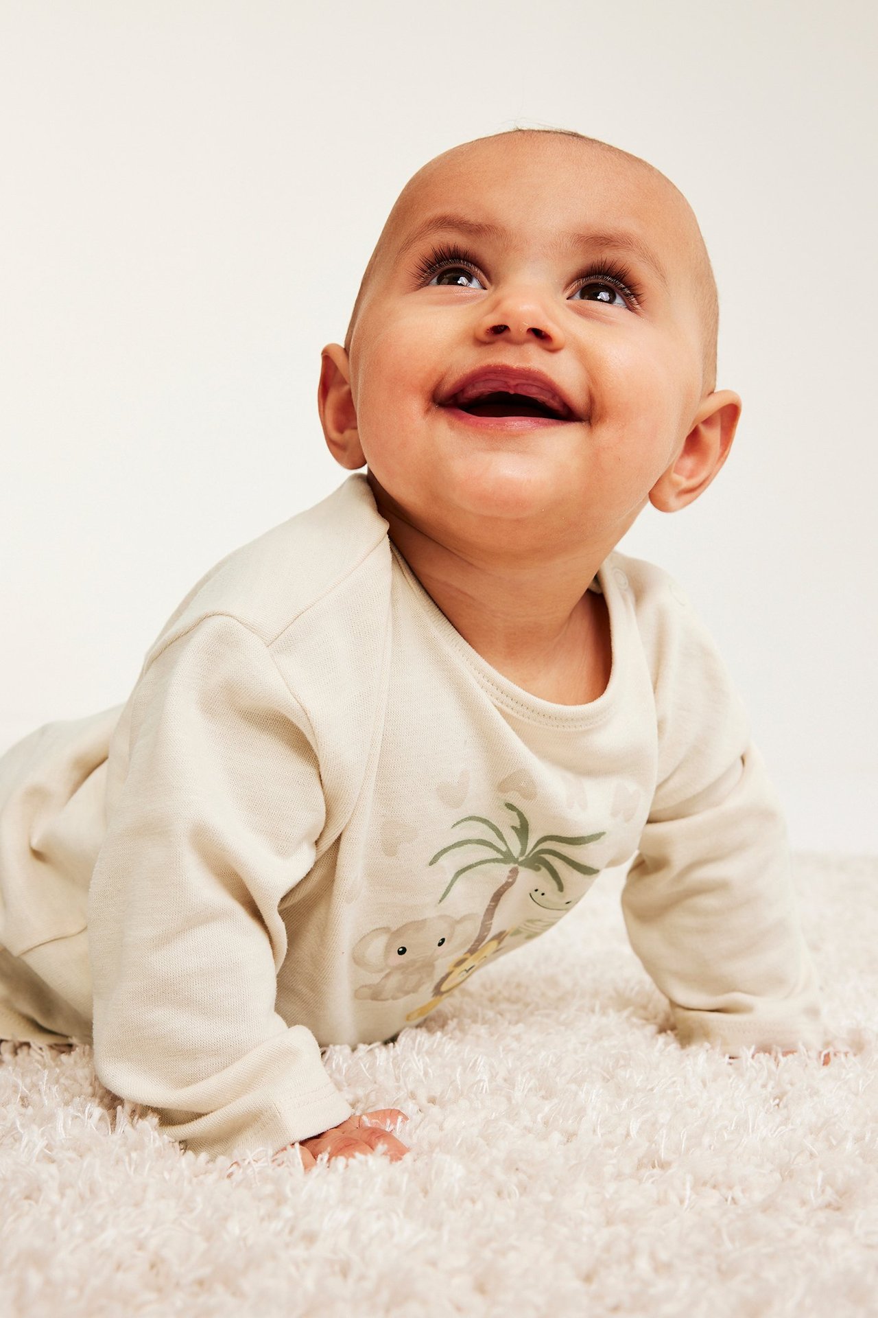 Edestä: Konttaava vauva yllään vaaleanbeige pitkähihainen puuvilla-t-paita eläinprintillä.