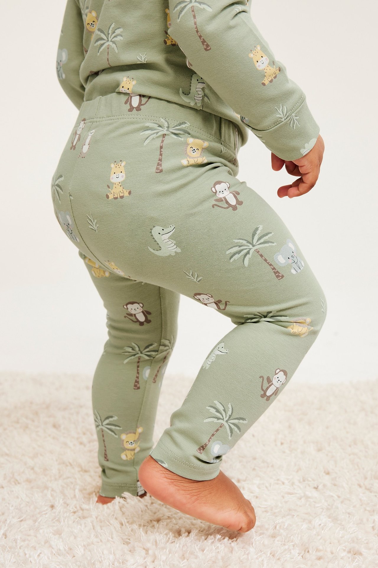 Takaapäin: Vauva vihreissä eläinkuvioiduissa leggingseissä ja yhteensopivassa pitkähihaisessa paidassa.