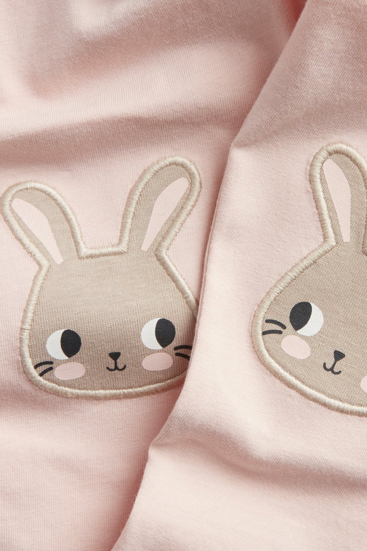 Närbild av babyrosa bomullsleggings med beiga kaninapplikationer på knäna.
