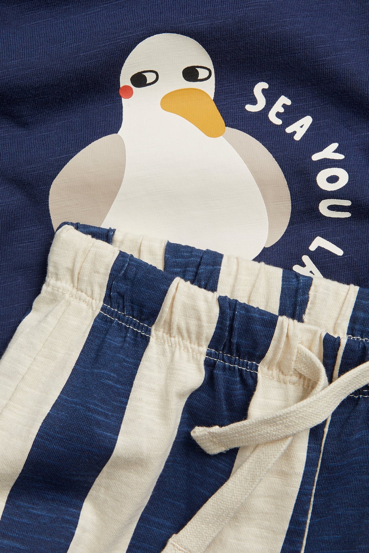 Närbild på en babys blå t-shirt med måstryck och blåvitrandiga joggingbyxor.