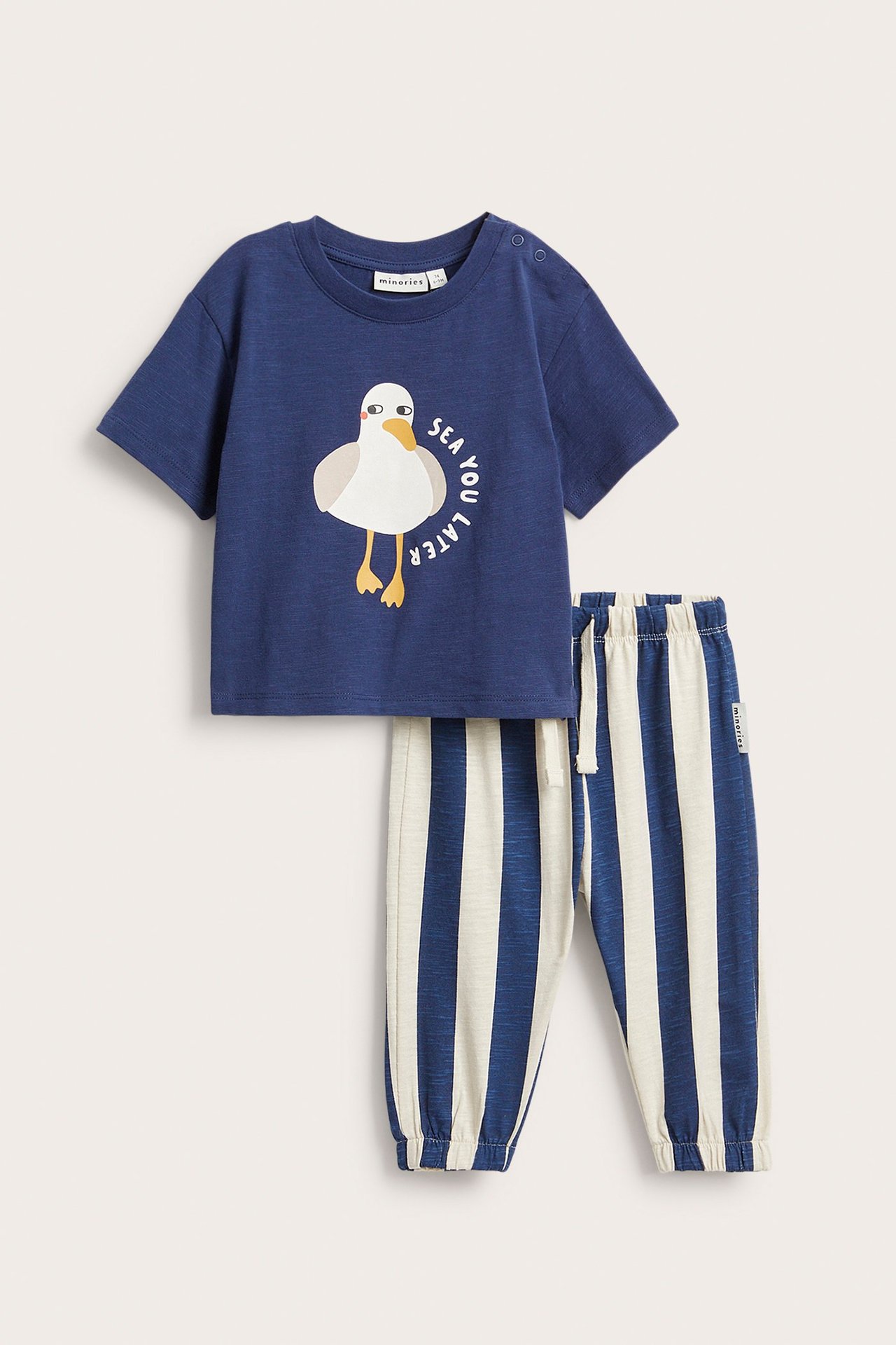 Frontvy av ett blått baby-t-shirt i bomull med ank-tryck och tryckknappar, matchad med randiga joggingbyxor.