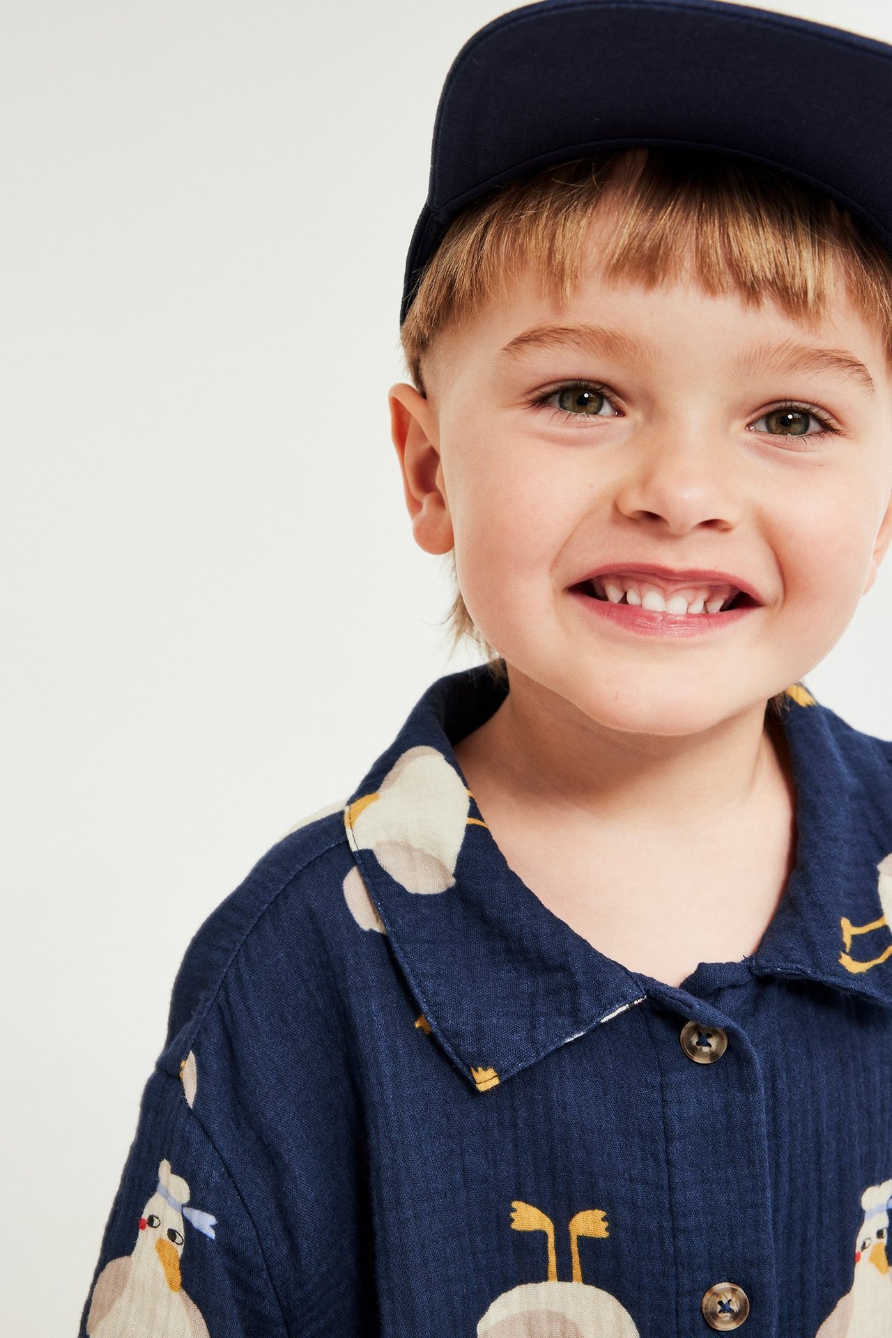 Smilende barn i blåmønstret kortermet musselin-skjorte med krage, knapper og marineblå caps.