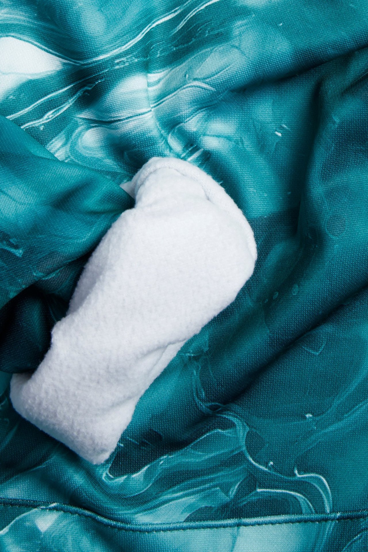 Zbliżenie na zieloną wzorzystą bluzę z kapturem z poliestru z białym puszystym podszewką widoczną w kieszeni kangurce.