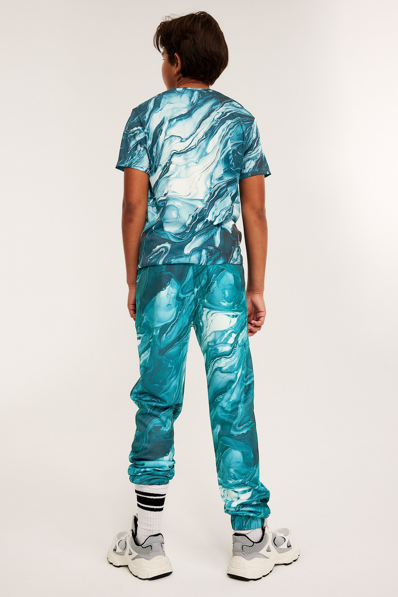 Widok od tyłu: dziecko w zielono-białych marmurkowych spodniach dresowych z poliestru i pasującym T-shircie.