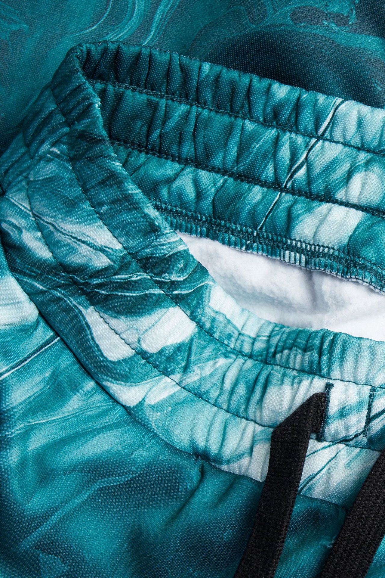 Zbliżenie: zielono-białe wzorzyste spodnie dresowe z poliestru z elastycznym pasem i czarnymi sznurkami.