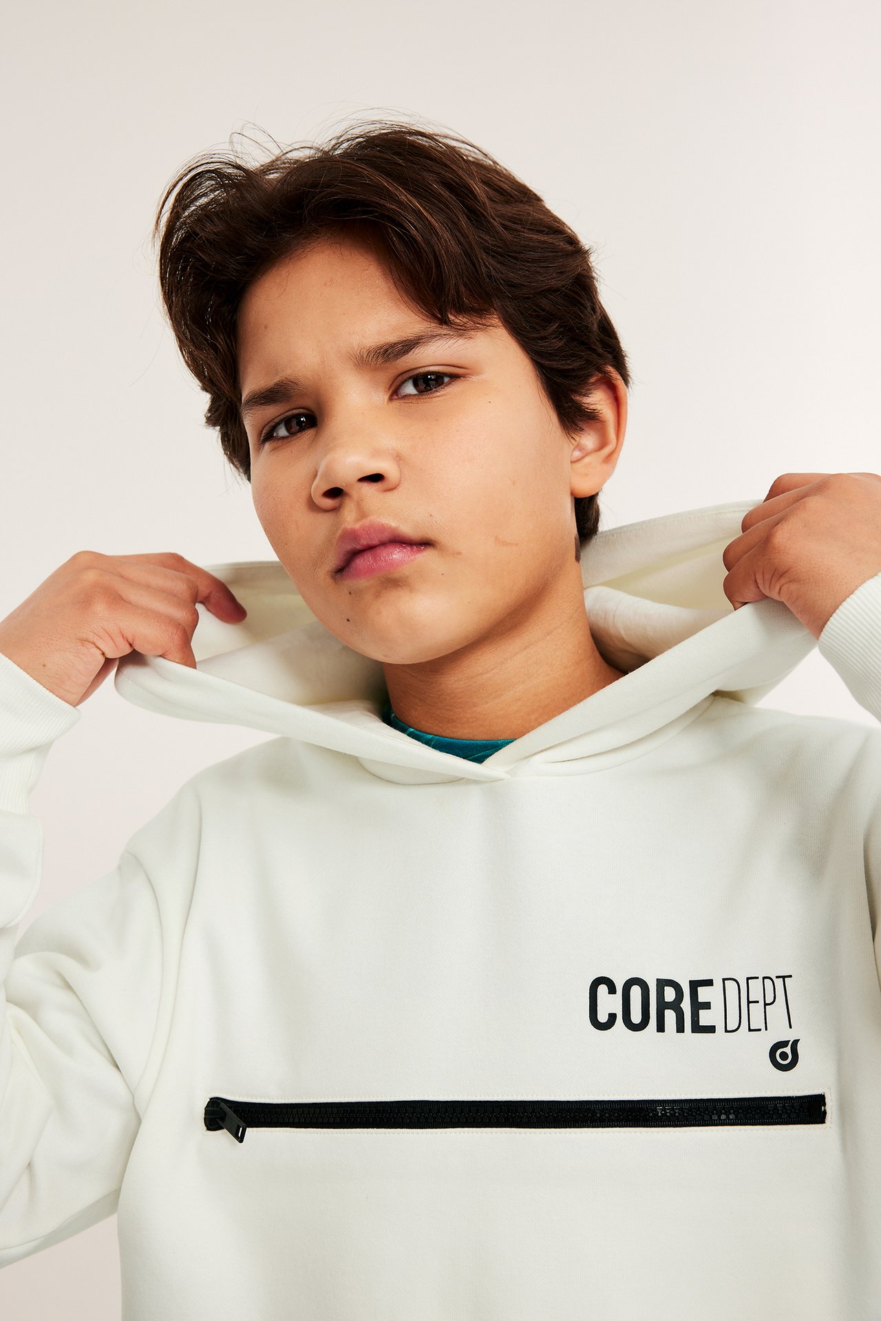 Widok z przodu: dziecko w białej bluzie z kapturem z czarnym zamkiem i nadrukiem 'CORE DEPT'.