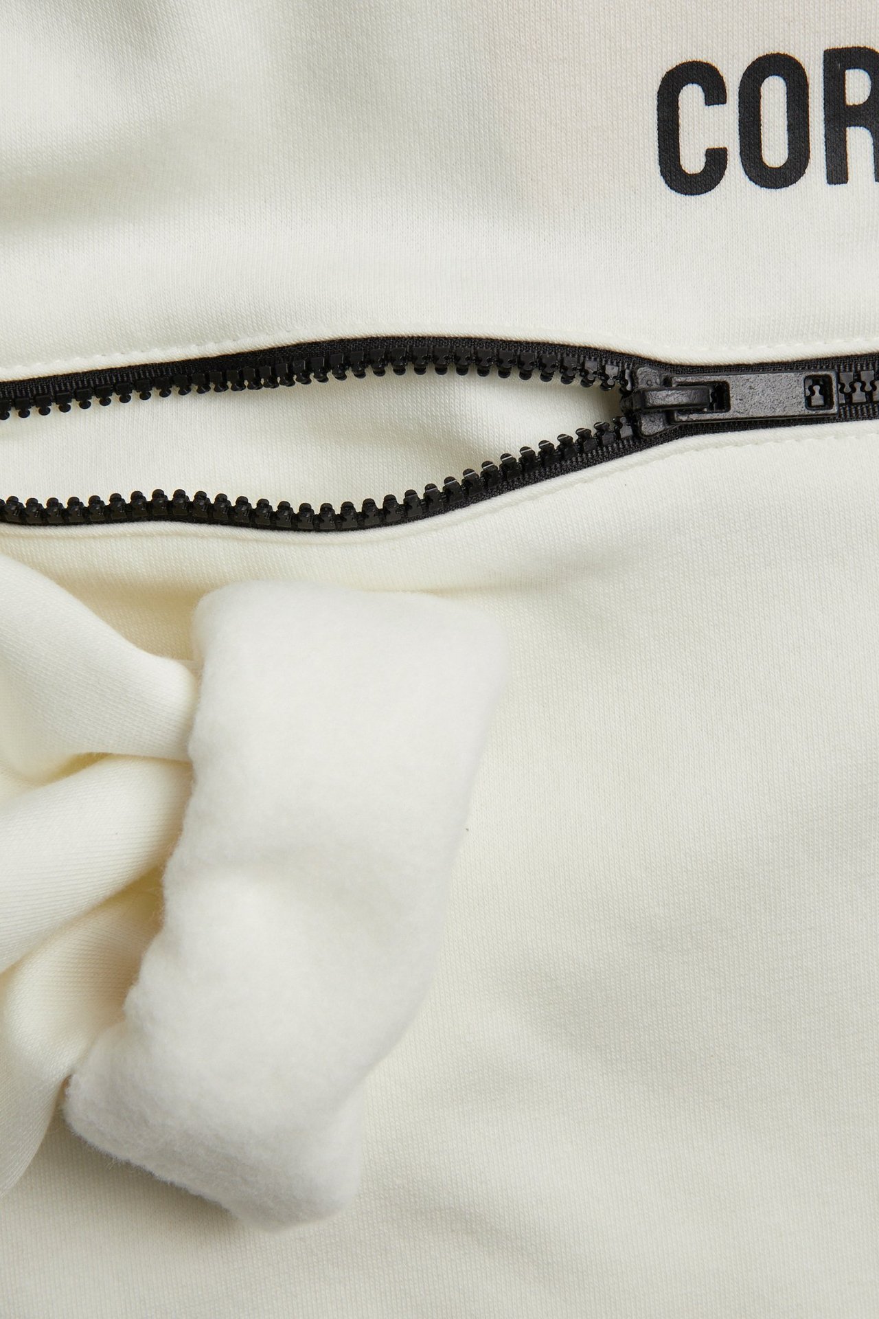 Zbliżenie na białą bluzę z kapturem z domieszką bawełny, czarnym zamkiem, zawiązanym sznurkiem i czarnym nadrukiem.