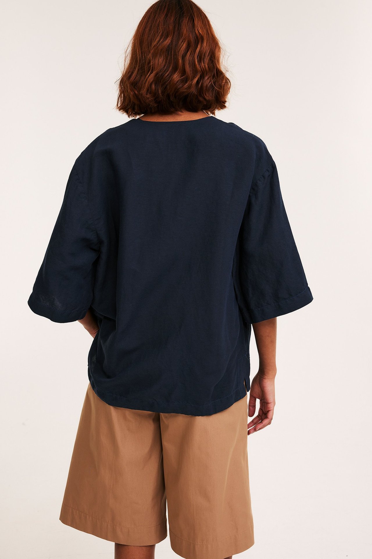 Ryggvy av en kvinna i mörkblå, lös kortärmad linneblandningsskjorta och beiga vida shorts.