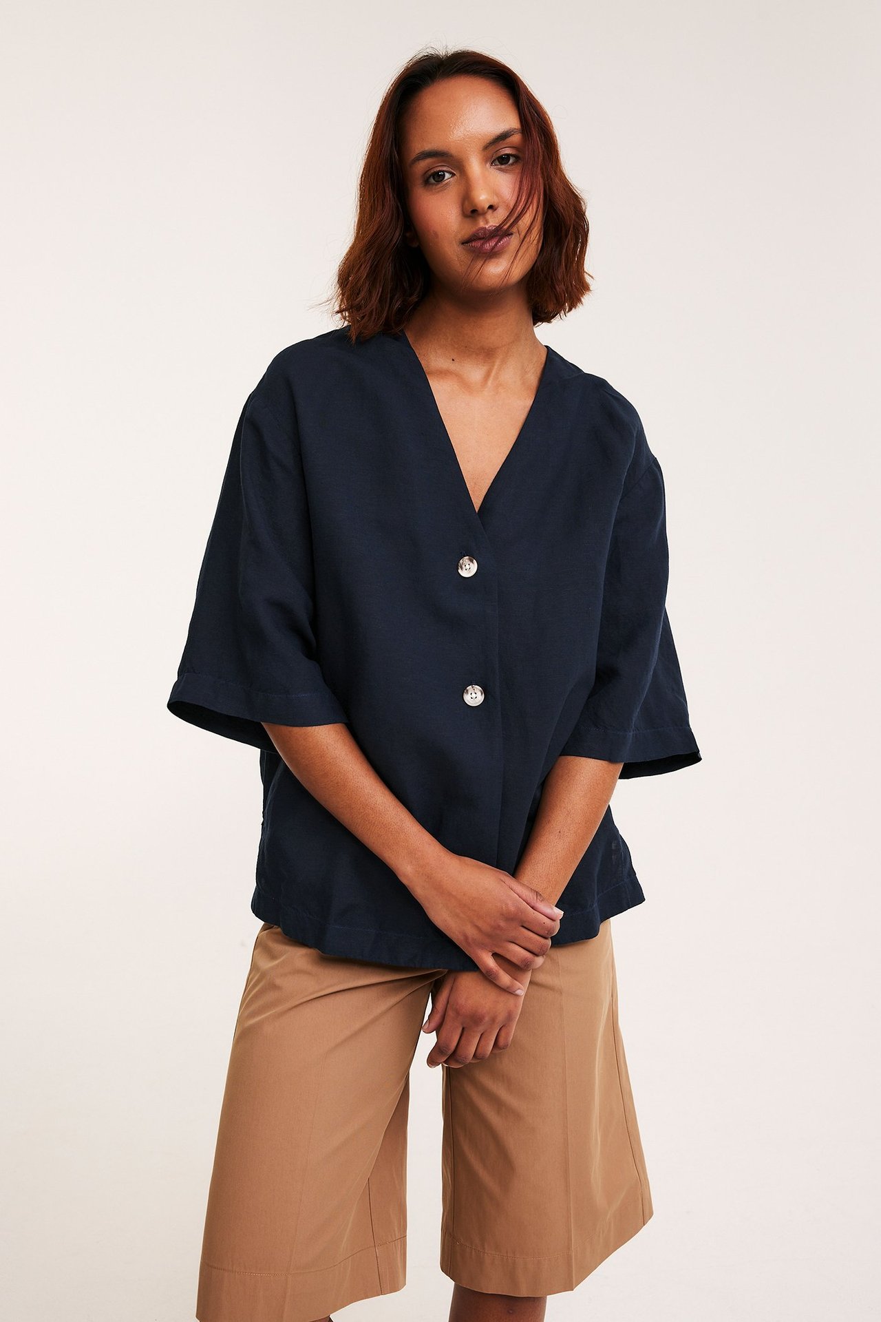 Kvinnans mörkblå linneblandning V-ringad skjorta med två knappar, buren med ljusbruna culottes. Framifrån.