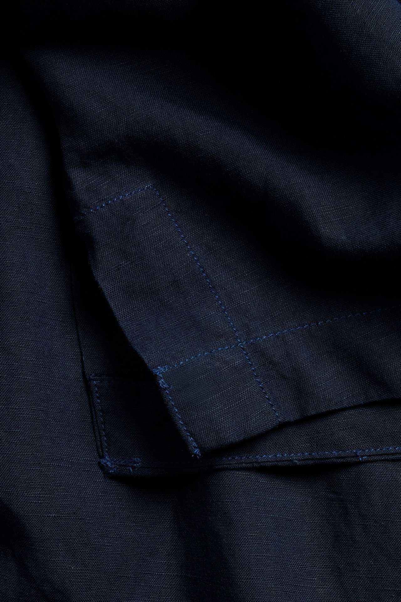 Närbild av mörkblå linneblandad skjortas tyg, som visar synliga blå dekorativa sömmar och textur.