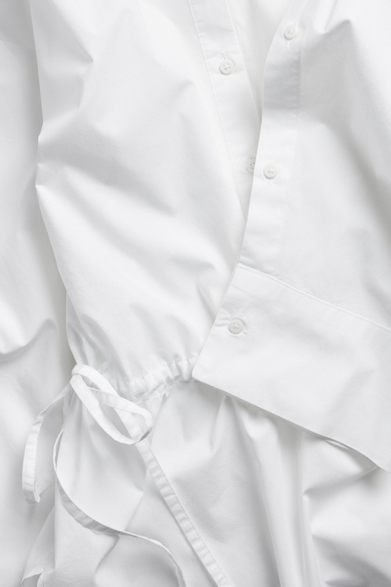 Zbliżenie białej koszuli z popeliny bawełnianej ze ściągaczem w talii i listwą guzikową.