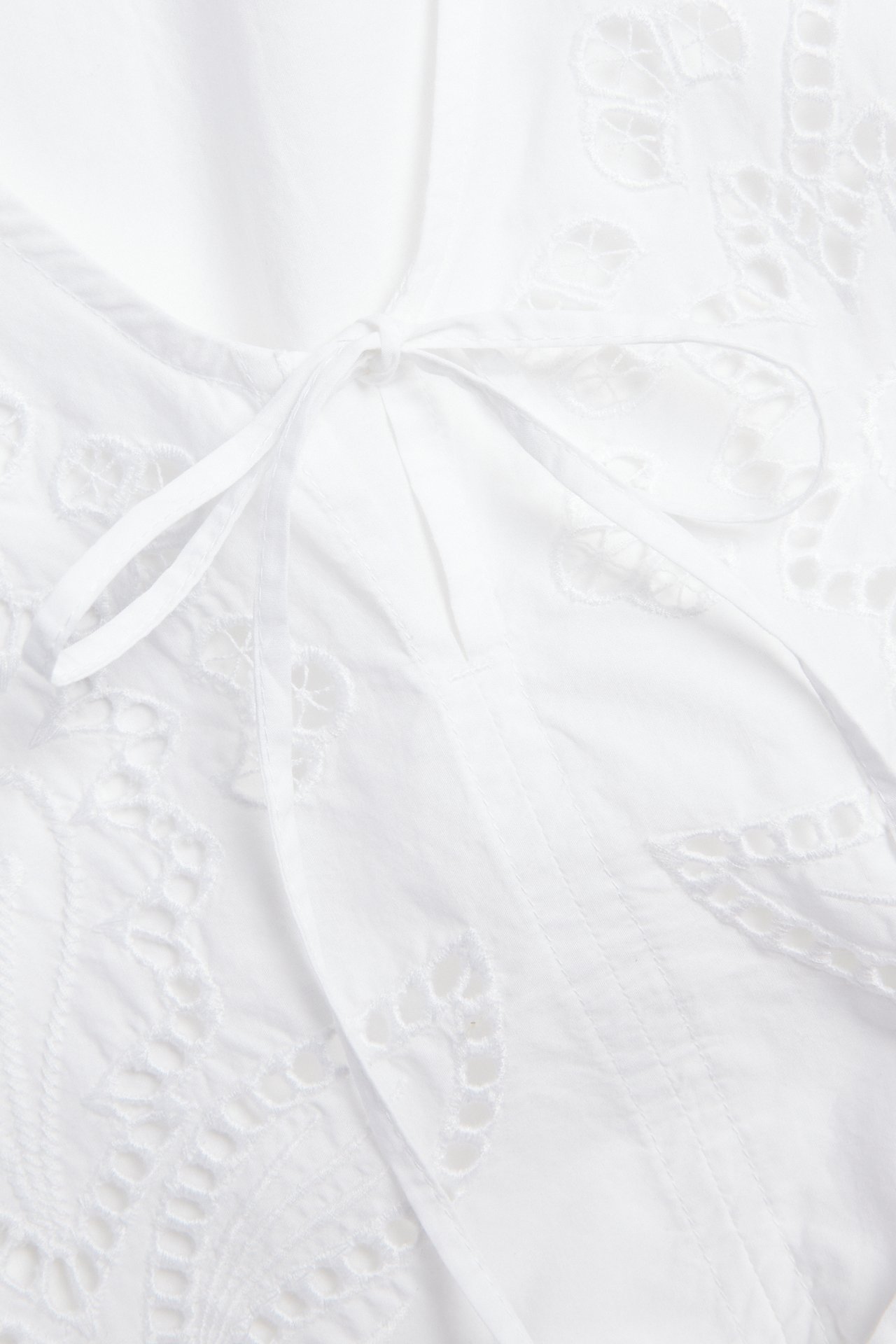 Zbliżenie białej bluzki z bawełnianej popeliny z haftem i widocznym wiązaniem na kokardę.