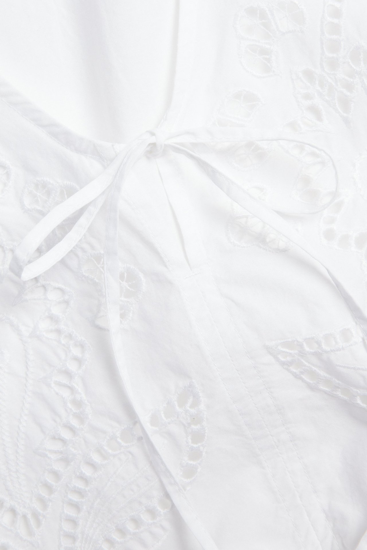 Lähikuva valkoisesta puuvillapopliinipuserosta, jossa on yksityiskohtaista kirjontaa ja solmimisnauha.