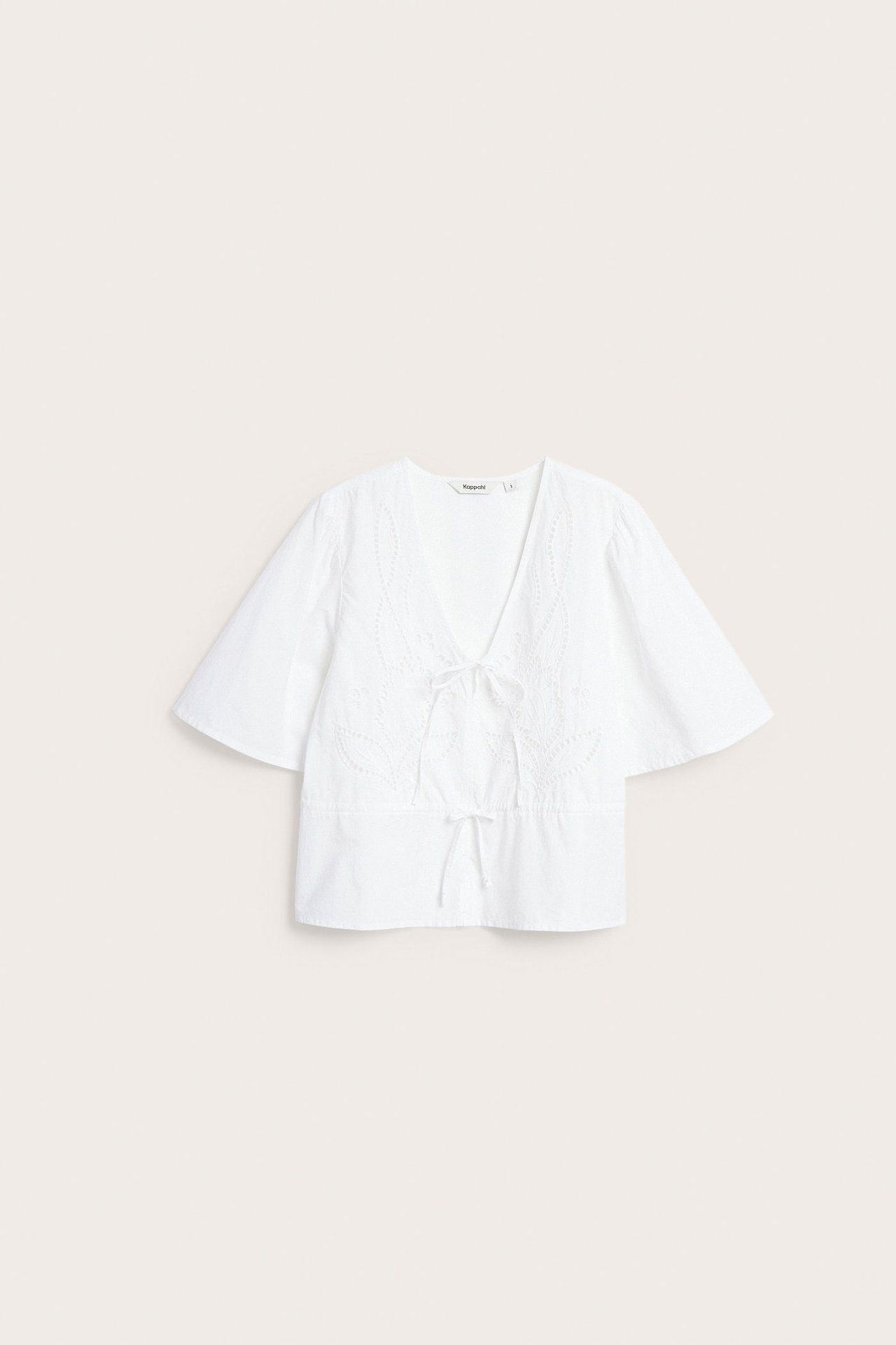 Edestä valkoinen puuvillapopliinipusero, brodeerattu V-pääntie, solmimisnauhat edessä ja nyöri vyötäröllä.