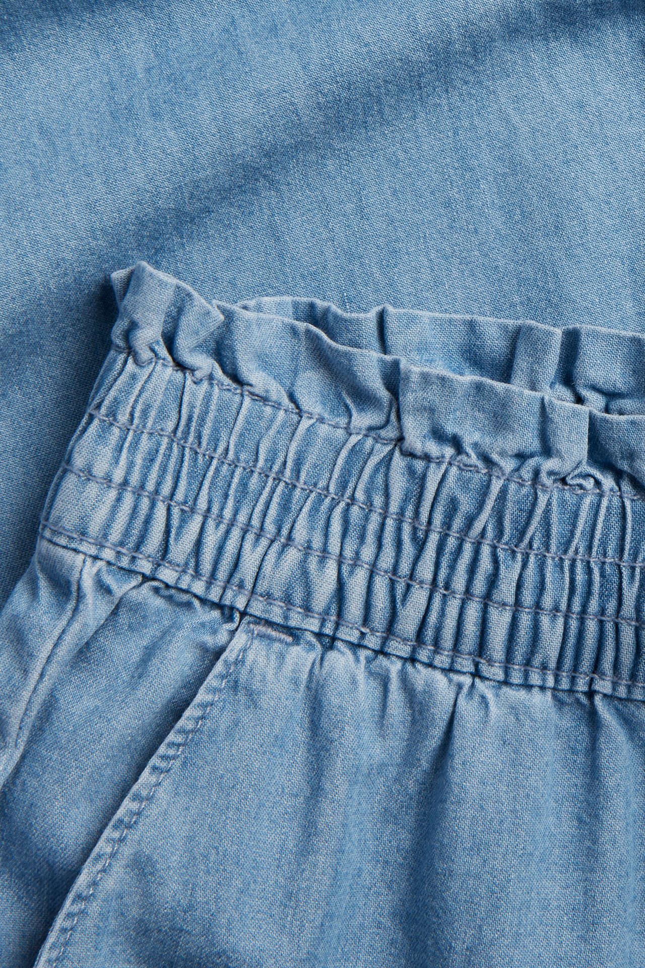 Zbliżenie na jasnoniebieskie dżinsowe spodnie dziecięce z elastyczną, marszczoną talią.