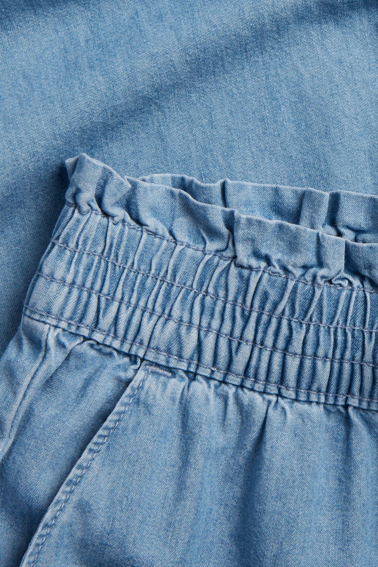 Närbild av barnens ljusblå denimbyxor med elastisk, rynkad midja.