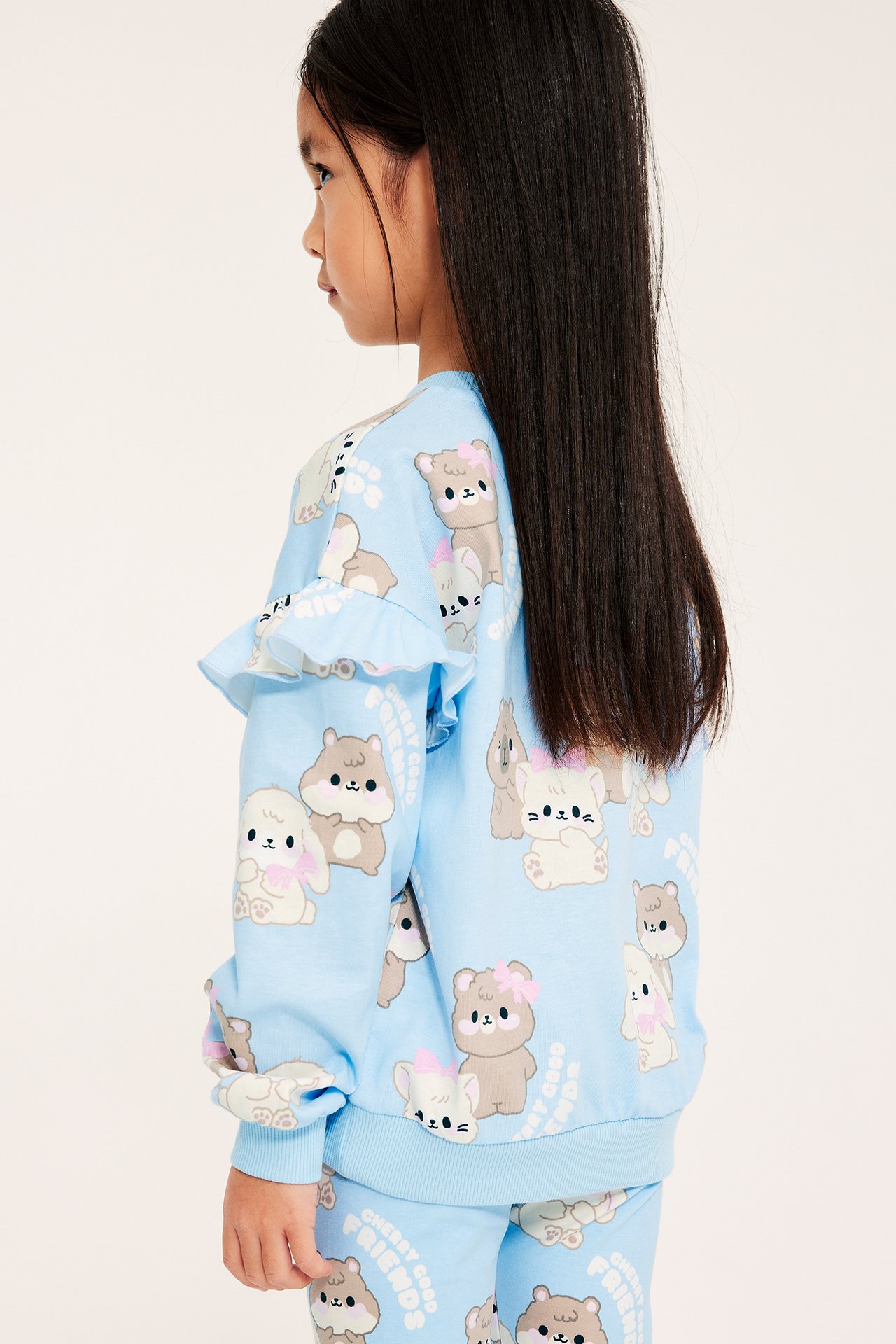 Widok z boku: dziecko w jasnoniebieskiej bluzie z nadrukiem zwierzęcym i falbankami.