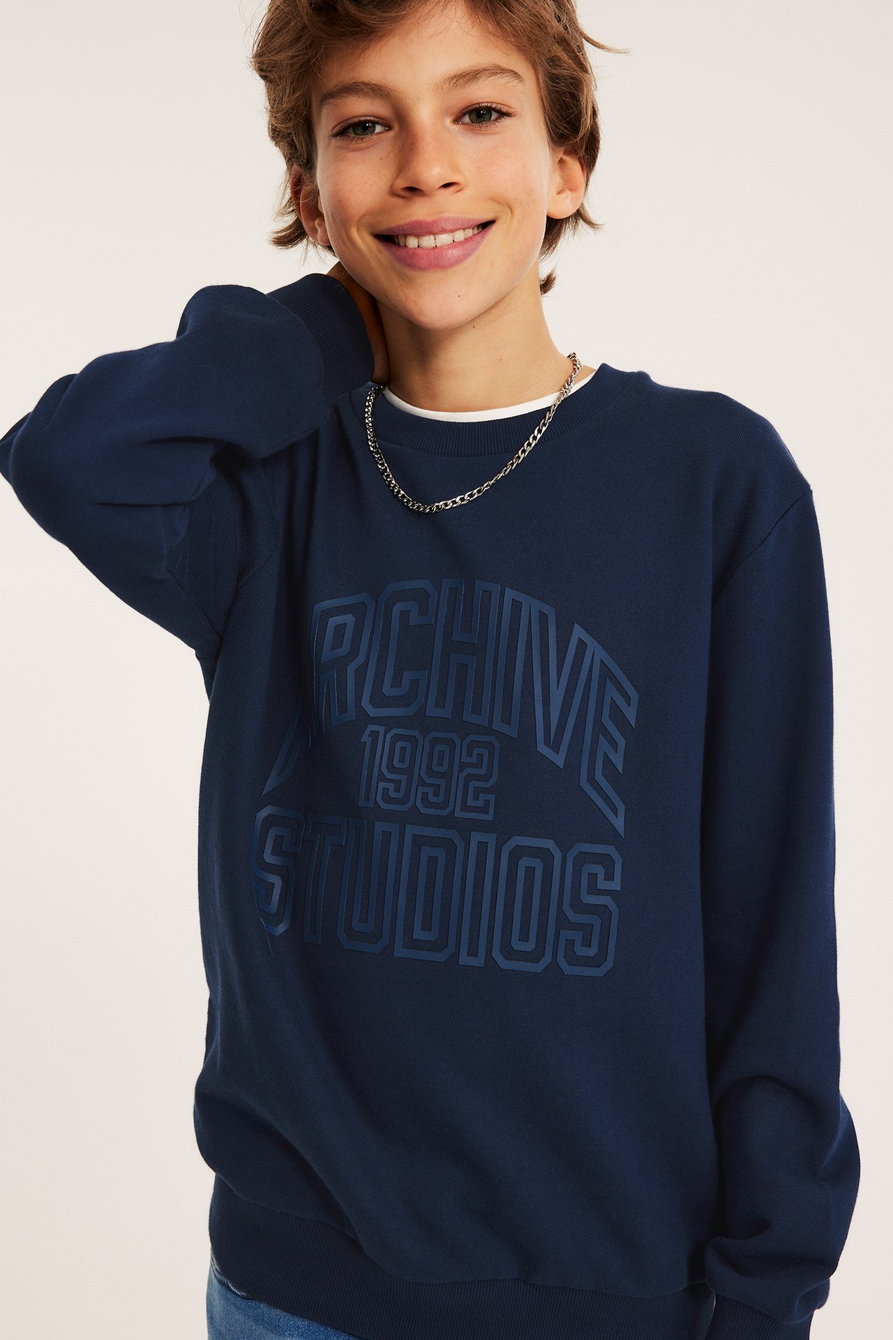 Widok z przodu: Dziecko nosi granatową bawełnianą bluzę z nadrukiem i srebrny łańcuszek.